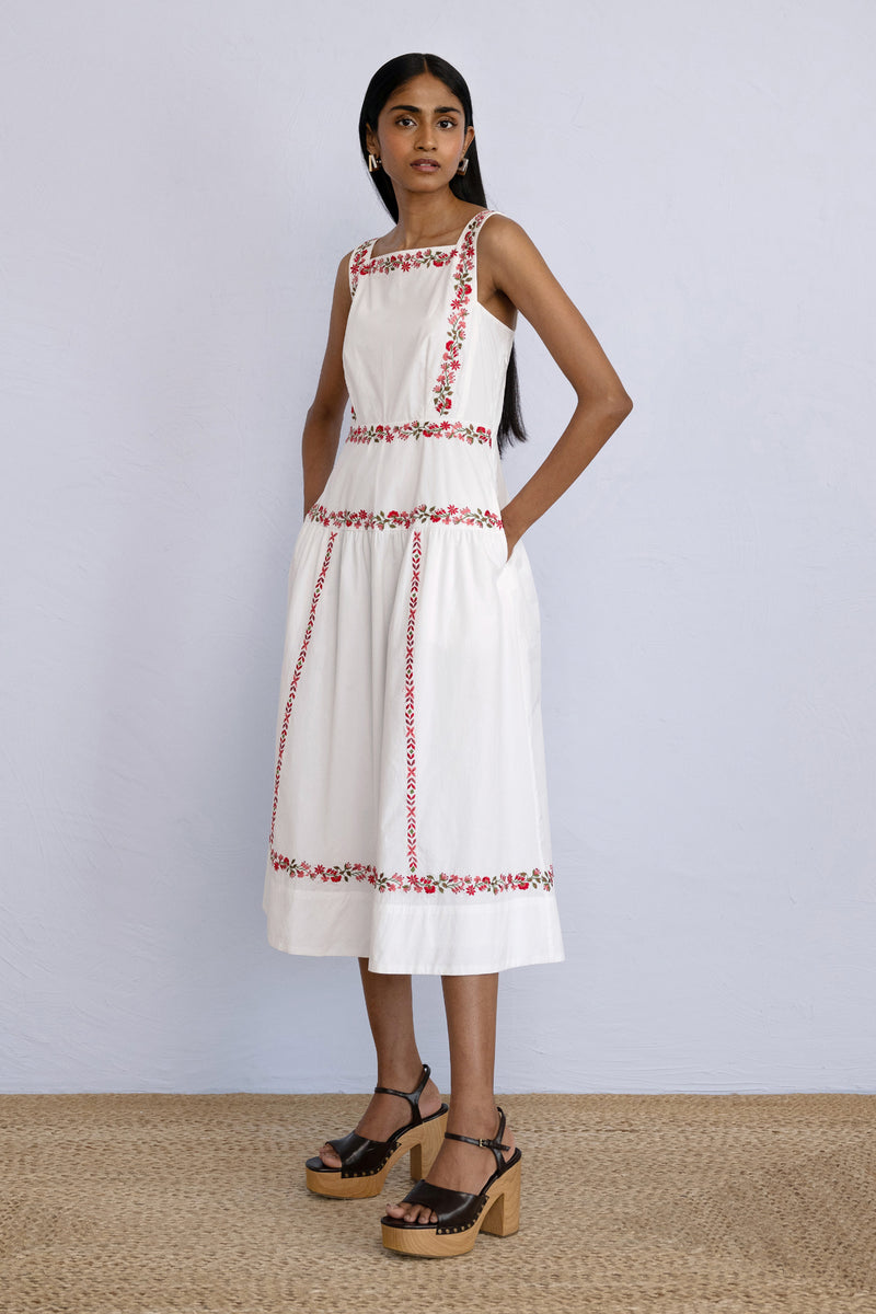 Model posing sideways wearing a midi length Rasia Dress Calico Embroidery Ivory Flame.