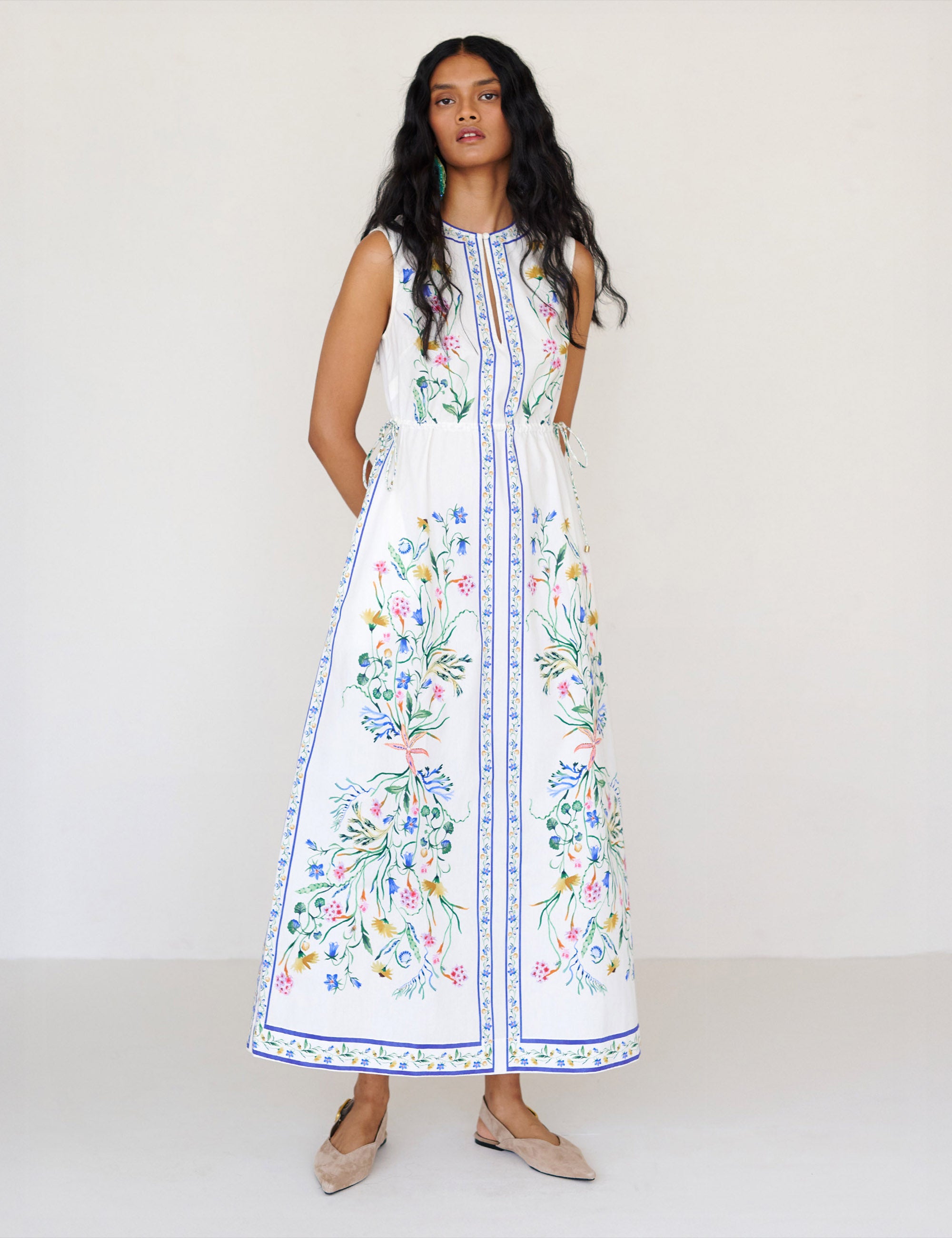 Front view of a woman standing. She is wearing the Rhonda column dress in Tidepool print. It features a crewneck with a fabric-covered button and keyhole detail, side drawstrings with gold caps, and side-seam pockets.