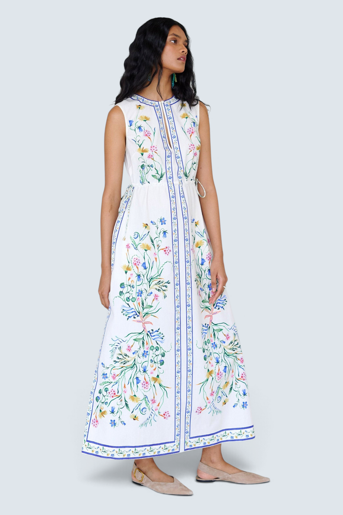 Front view of a woman standing looking sideways. She is wearing the Rhonda column dress in Tidepool print. It features a crewneck with a fabric-covered button and keyhole detail, side drawstrings with gold caps, and side-seam pockets.