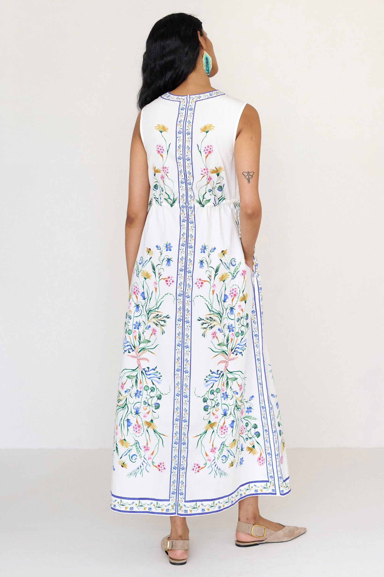 Back view of a woman standing wearing the Rhonda column dress in Tidepool print, featuring side drawstrings with gold caps, front keyhole button, and side-seam pockets.