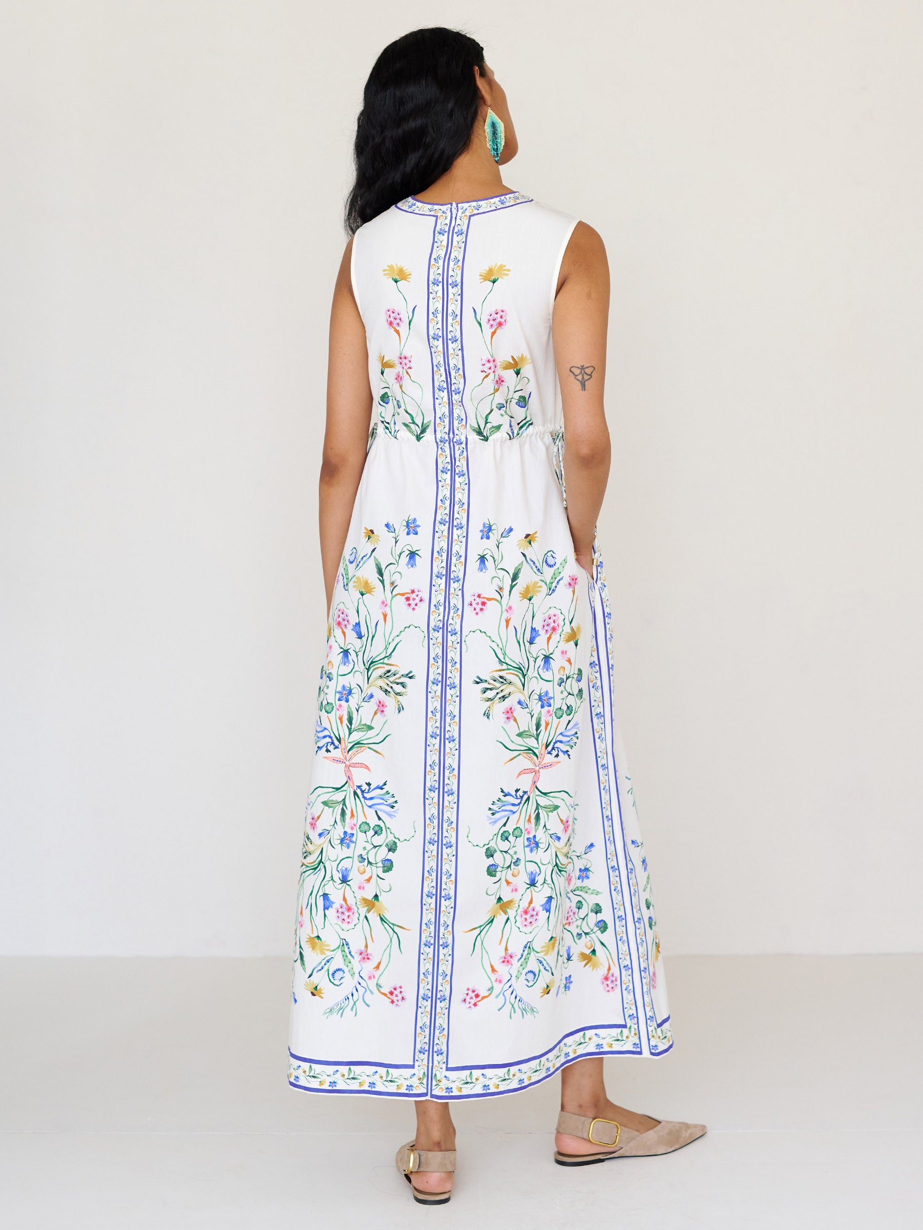 Back view close up of a woman standing. She is wearing the Rhonda column dress in Tidepool print. It features a crewneck with a fabric-covered button and keyhole detail, side drawstrings with gold caps, and side-seam pockets.