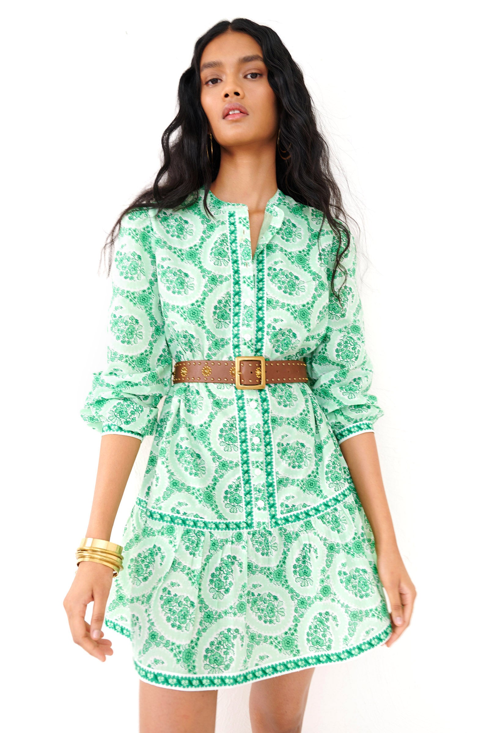 Front view close up of a woman standing. She is  wearing the Roma mini shirtdress in Paisley Copse print styled with a brown belt, stack of gold bracelets and ear rings.