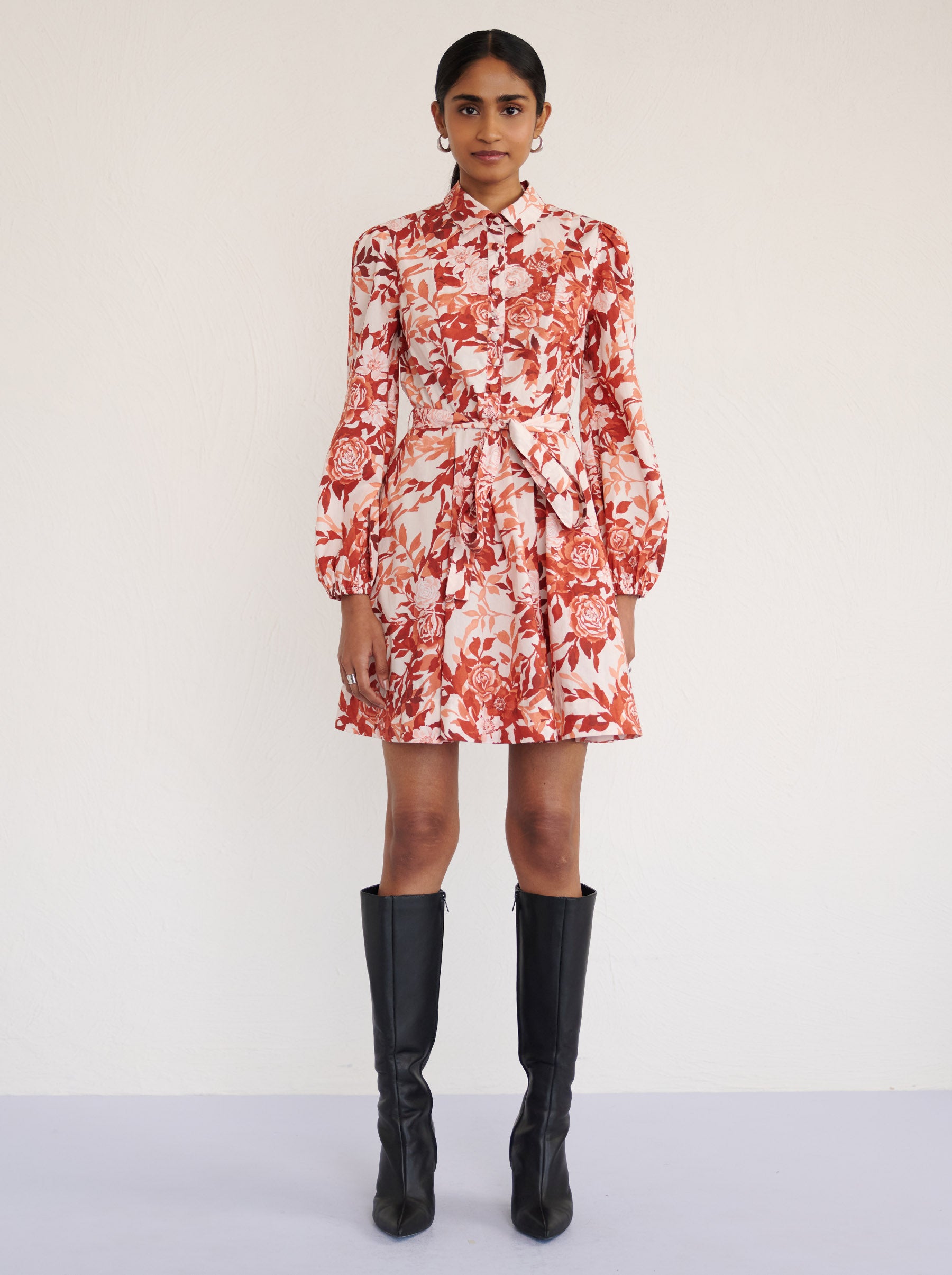 Front view of a model standing. She is wearing the Rowena mini shirtdress in crisp cotton poplin in Bibi Rose Chocolate print. It is featuring a delicate collar, lantern sleeves, short hem, full lining, and side-seam pockets.