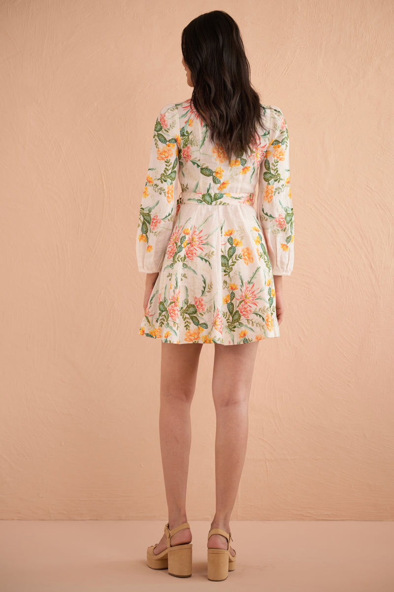Back view of woman wearing Rowena Dress in Desert Rose Dawn print, a mini linen shirtdress with delicate collar, fabric-covered buttons, elegant lantern sleeves, and side-seam pockets featuring watercolor-style cactus flowers.