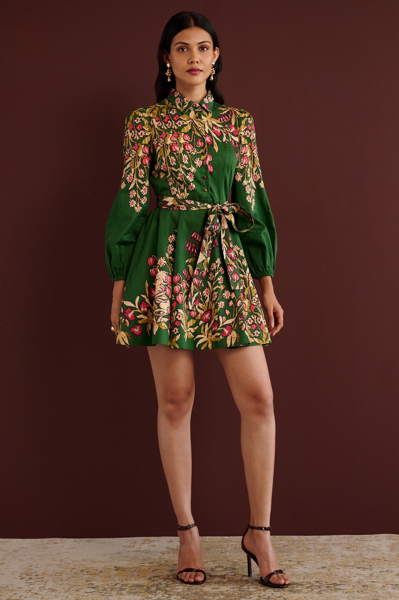 Front view of woman standing. She is wearing the Rowena mini shirtdress in Unicorn Tapestry print. It features a fitted bodice, delicate collar, lantern sleeves, short hem, side-seam pockets, and 15th-century-inspired enchanted garden motifs from the Scottish Highlands.