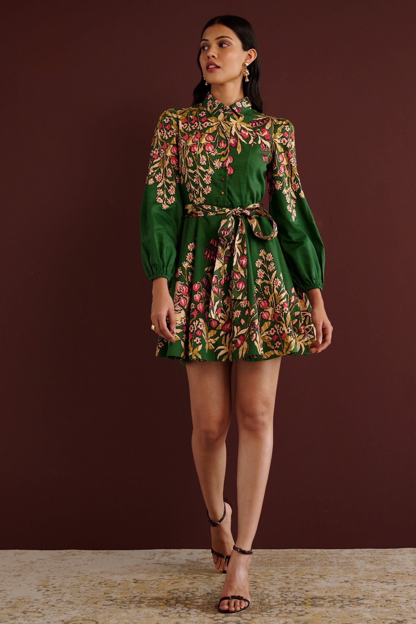 Front view of woman walking. She is wearing the Rowena mini shirtdress in Unicorn Tapestry print. It features a fitted bodice, delicate collar, lantern sleeves, short hem, side-seam pockets, and 15th-century-inspired enchanted garden motifs from the Scottish Highlands.