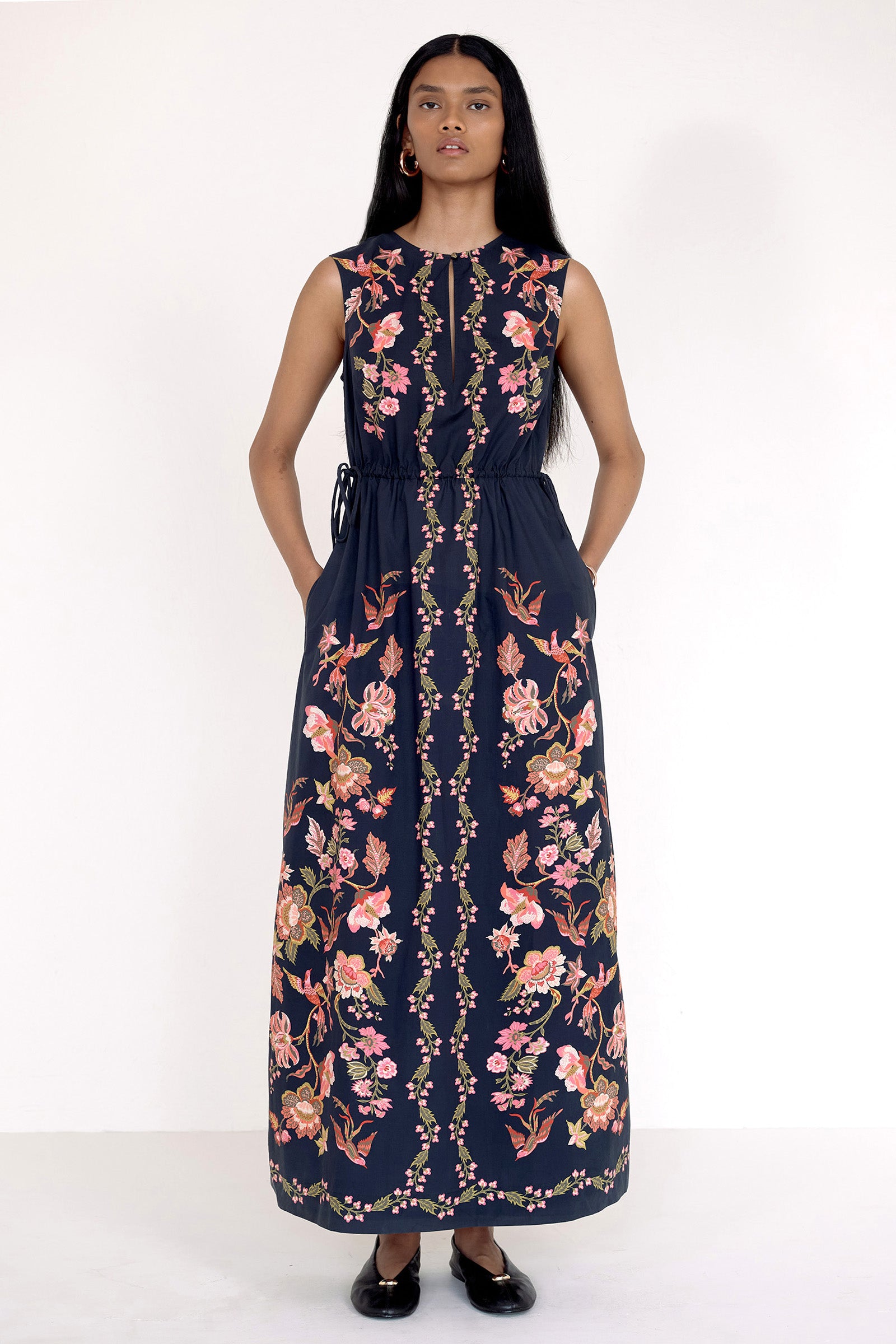 Front view of model standing. She is wearing the Rhonda dress in Chintz Jet with hands in pocket. It features a crewneck with keyhole detail, adjustable drawstring sleeves, column silhouette, and vintage-inspired floral and bird print.