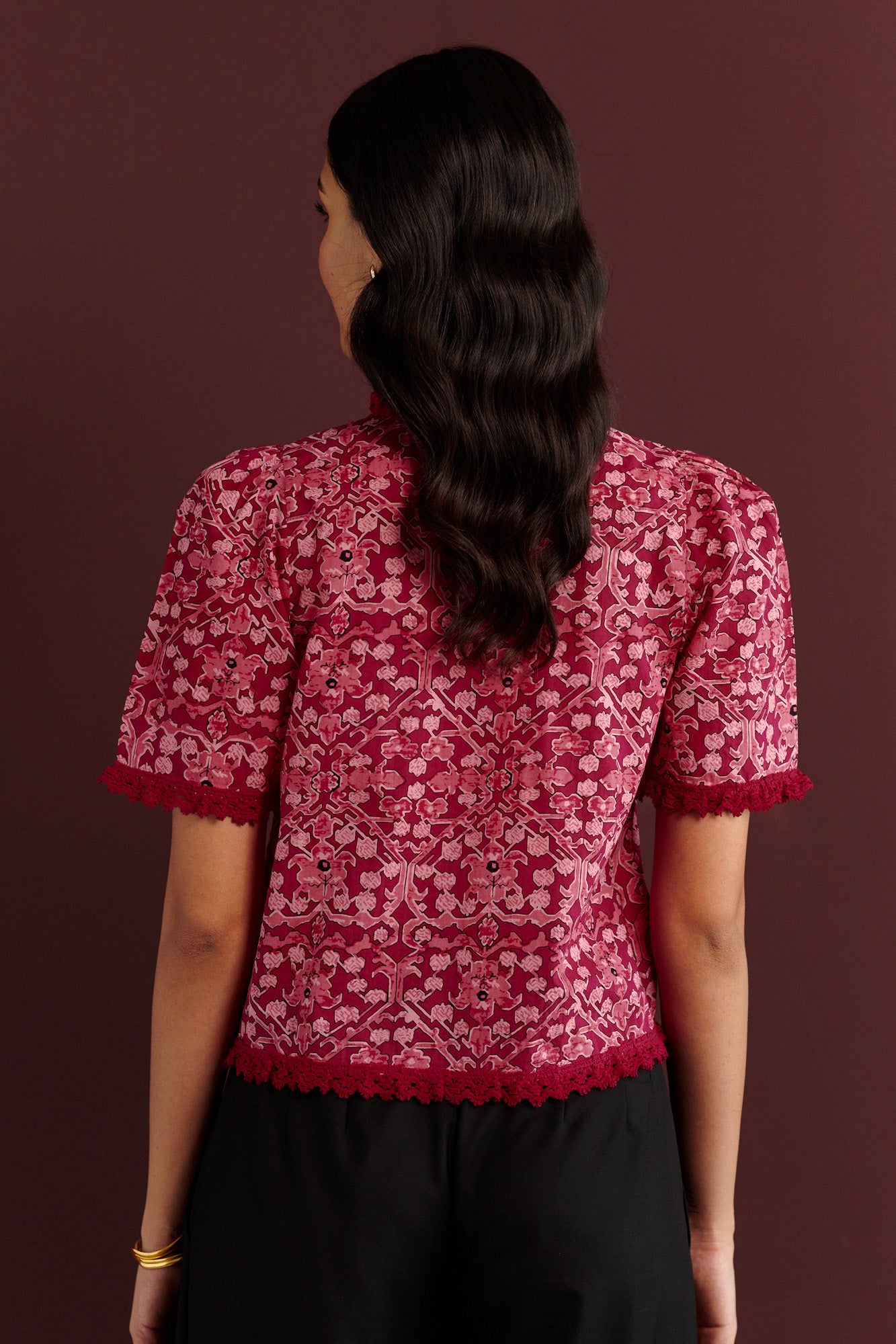 Front view of woman standing. She is wearing the Sarah top in the Ottoman print. It is a Berry red cotton cambric blouse with red lace trim styled for a festive and elegant winter look.