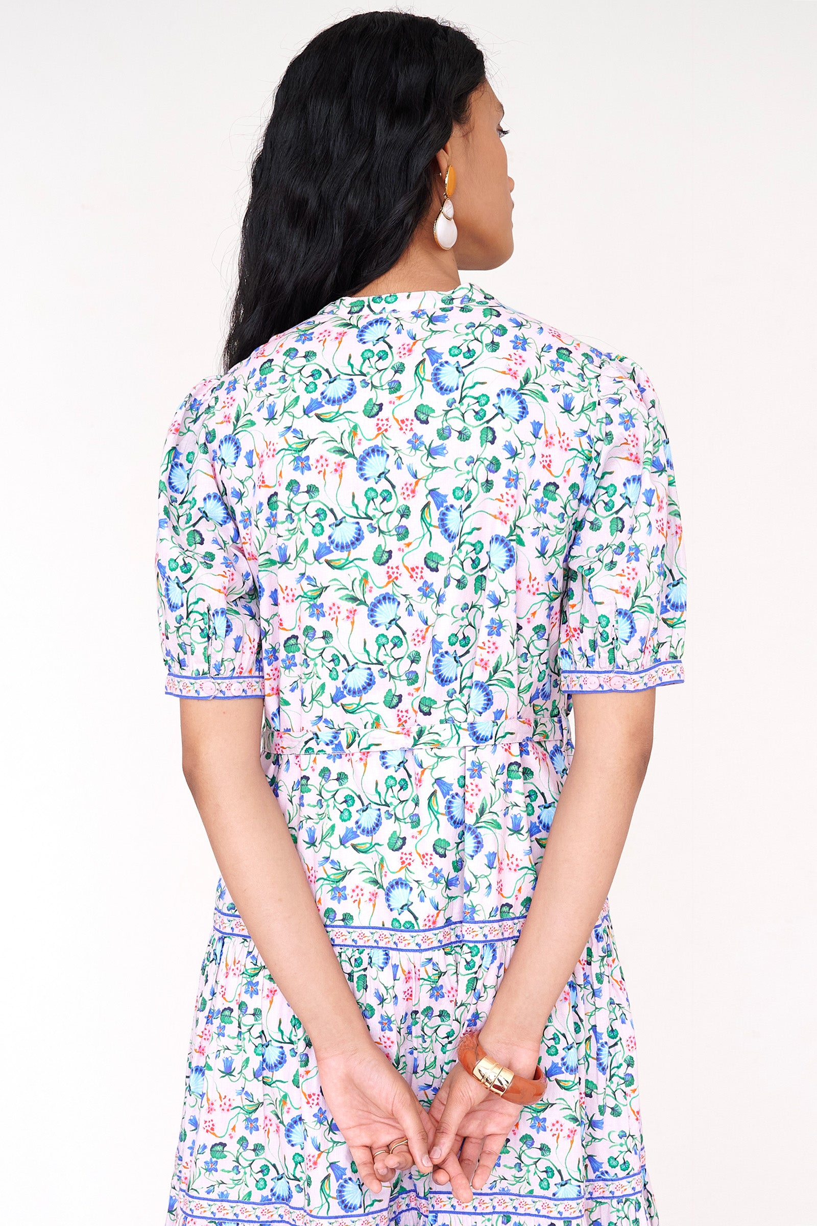 Back view close up of a woman standing wearing the Saylor dress in Clam Garland print. It features a stand collar, contrast trim, tiered skirt, detachable belt, and full-length shirtdress silhouette.