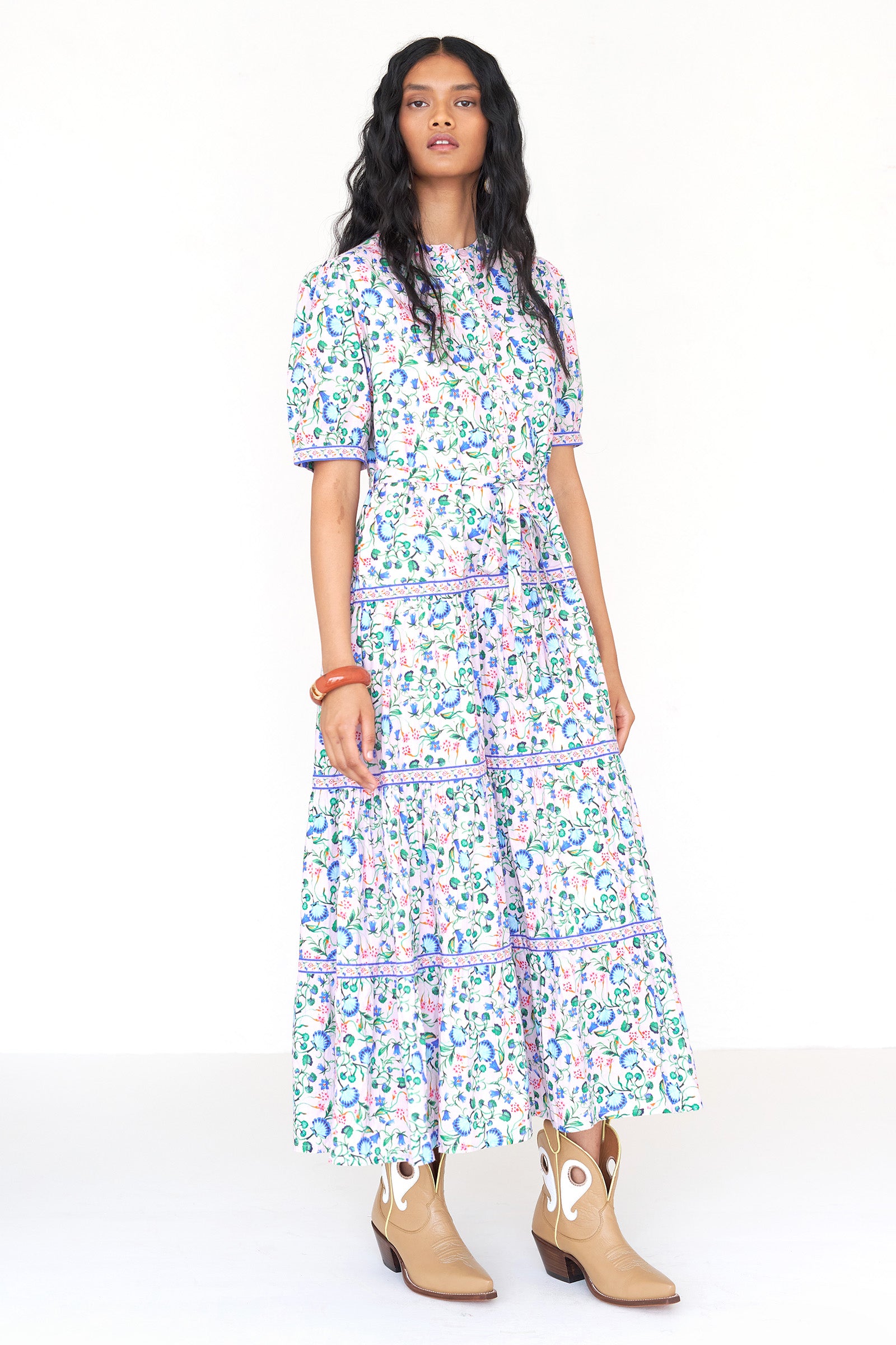 Front side view of a woman standing wearing the Saylor dress in Clam Garland print. It features a stand collar, contrast trim, tiered skirt, detachable belt, and full-length shirtdress silhouette.