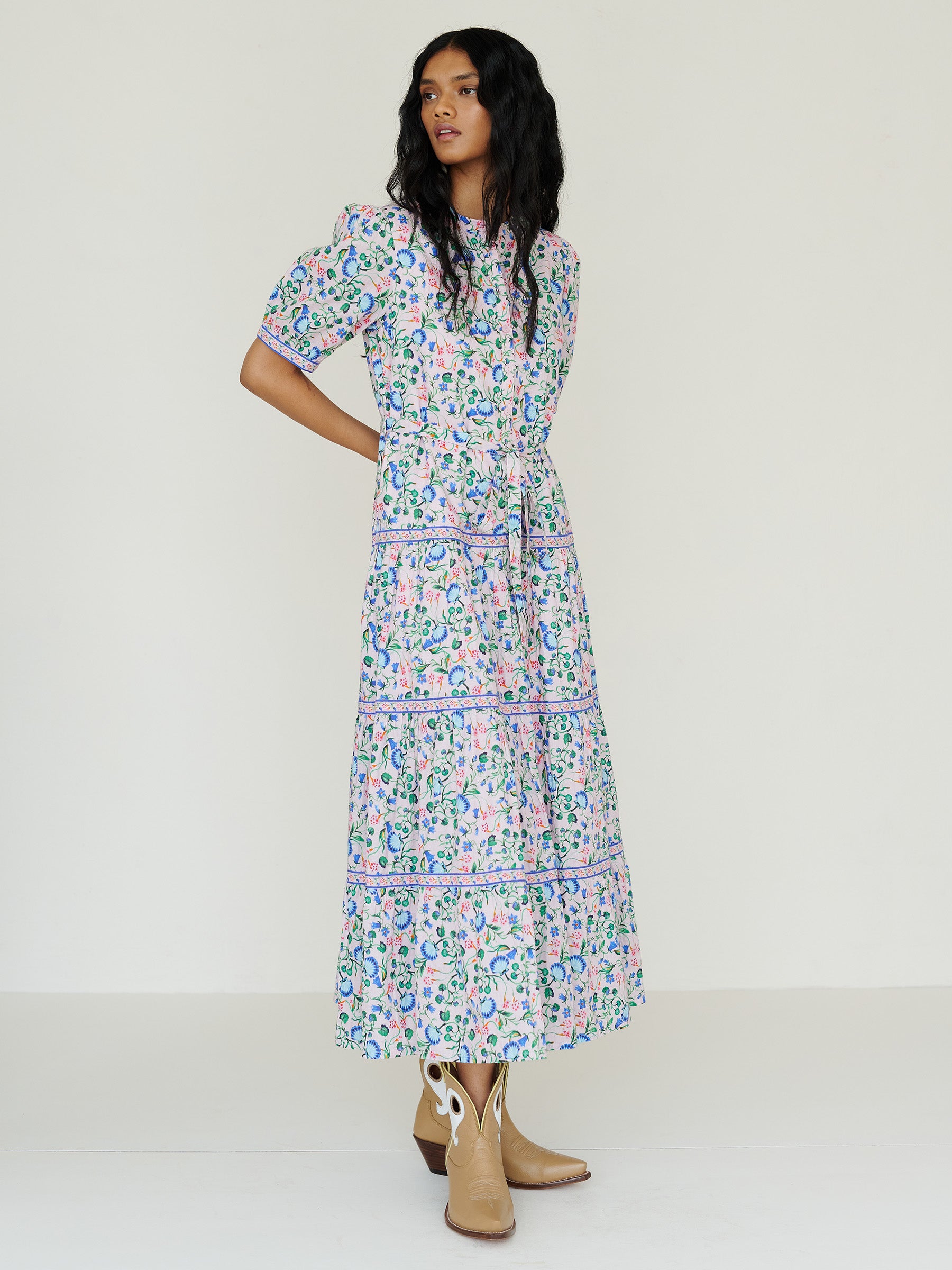 Side view of a woman standing. She is  wearing the Saylor dress in Clam Garland floral print. It features a classic shirtdress design with stand collar, tiered skirt, contrast trim, and a detachable belt.
