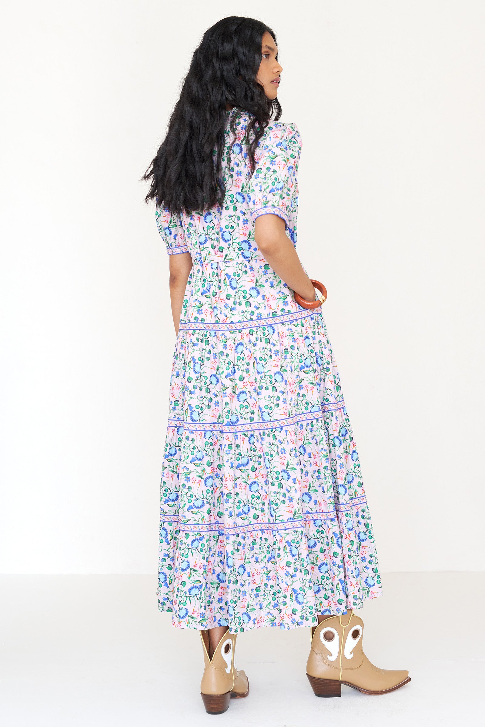 Back view of a woman standing wearing the Saylor dress in Clam Garland print. It features a stand collar, contrast trim, tiered skirt, detachable belt, and full-length shirtdress silhouette.