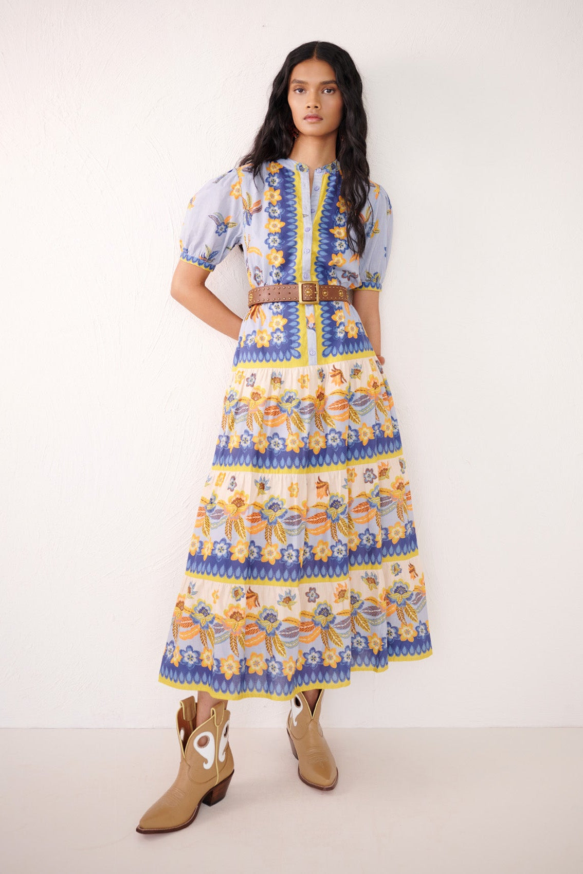 Front view of woman standing. She is wearing Saylor Shirt dress in Electra Floral  Amberglow print with geometric and floral motifs, featuring full-length skirt and detachable belt.