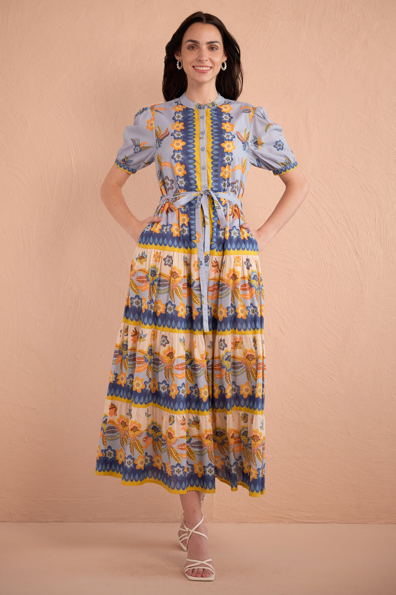 Front view of woman wearing floral print midi dress with short puff sleeves, tiered skirt, and tie waist in amber, blue, and yellow tones.