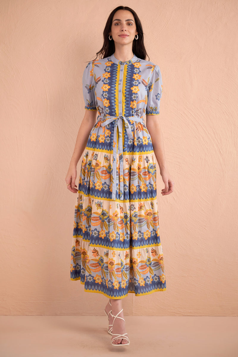 Front view of woman wearing floral print midi dress with short puff sleeves, tiered skirt, and tie waist in amber, blue, and yellow tones.