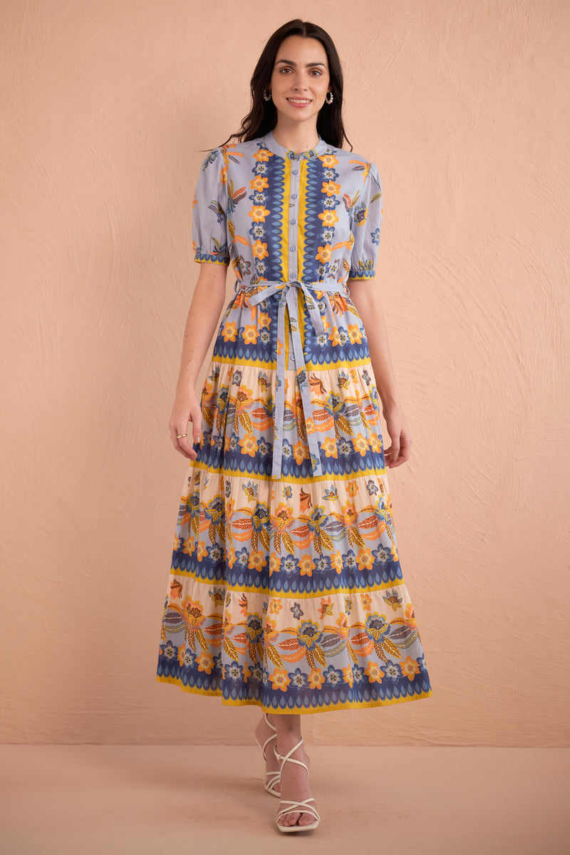 Front view of woman wearing floral print midi dress with short puff sleeves, tiered skirt, and tie waist in amber, blue, and yellow tones.