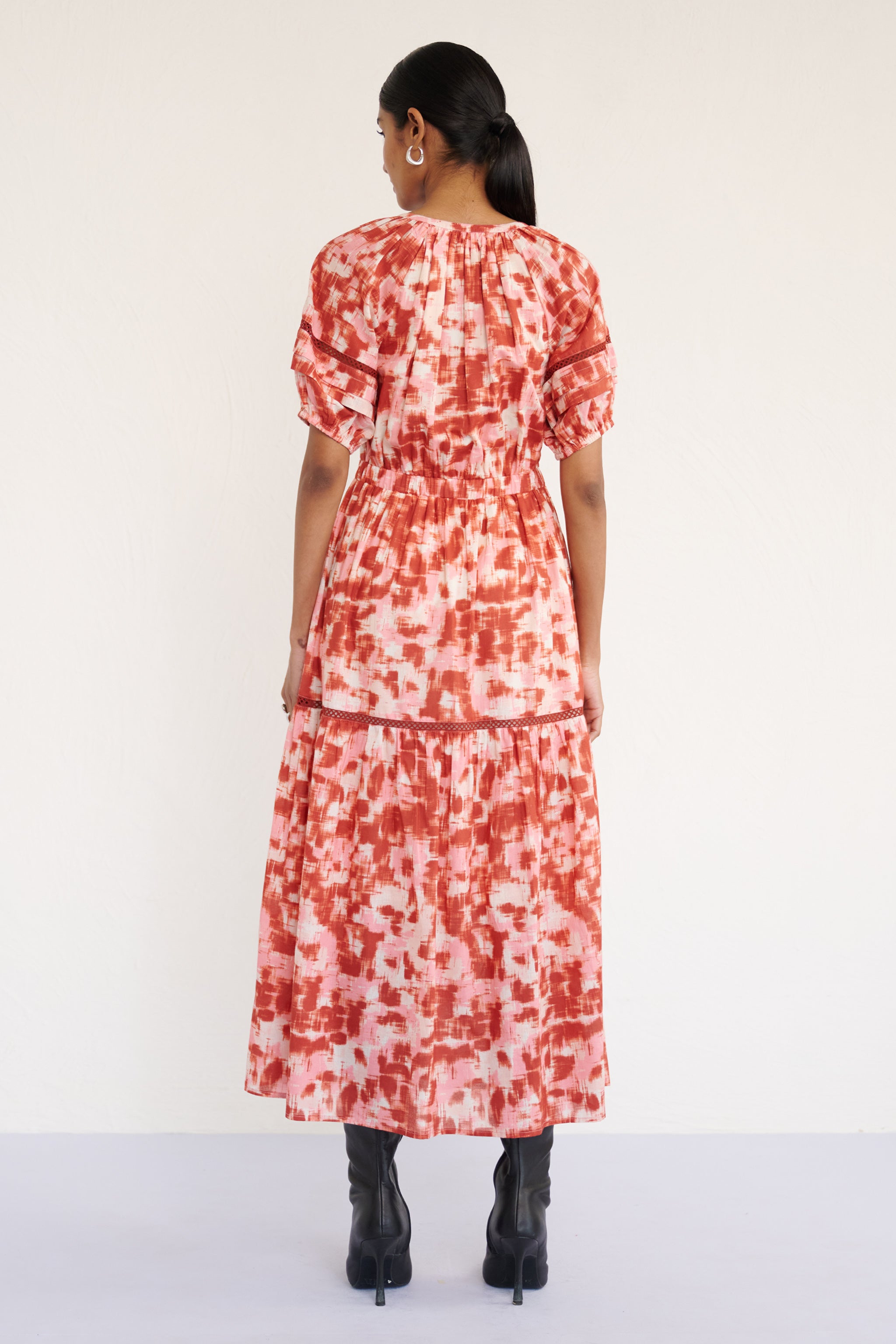 Back view of woman wearing a full-length V-neck dress with tie-neck detail, lace inserts on the skirt and sleeves, and an ikat-inspired animal print.