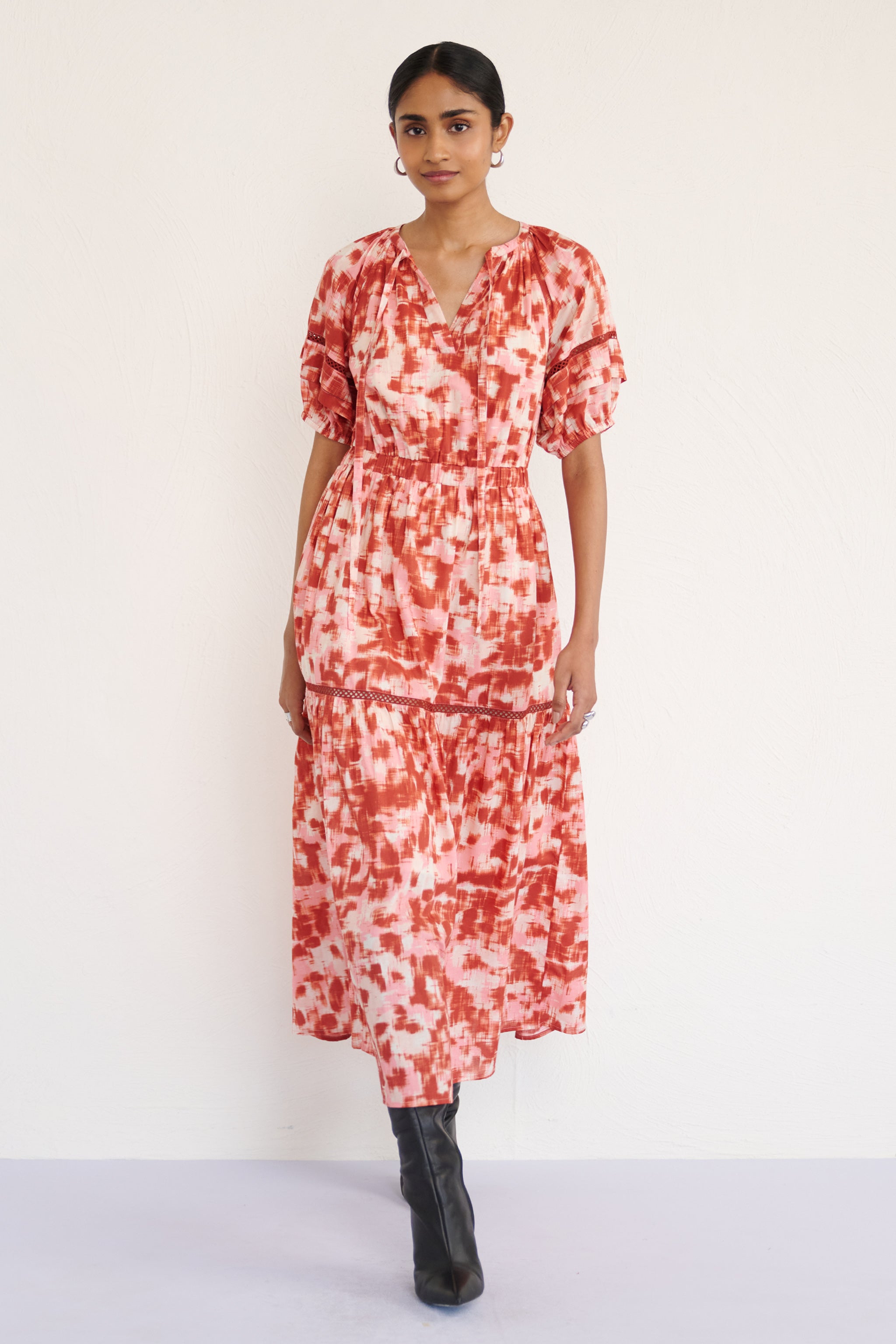 Front view of woman wearing a full-length V-neck dress with tie-neck detail, lace inserts on the skirt and sleeves, and an ikat-inspired animal print.