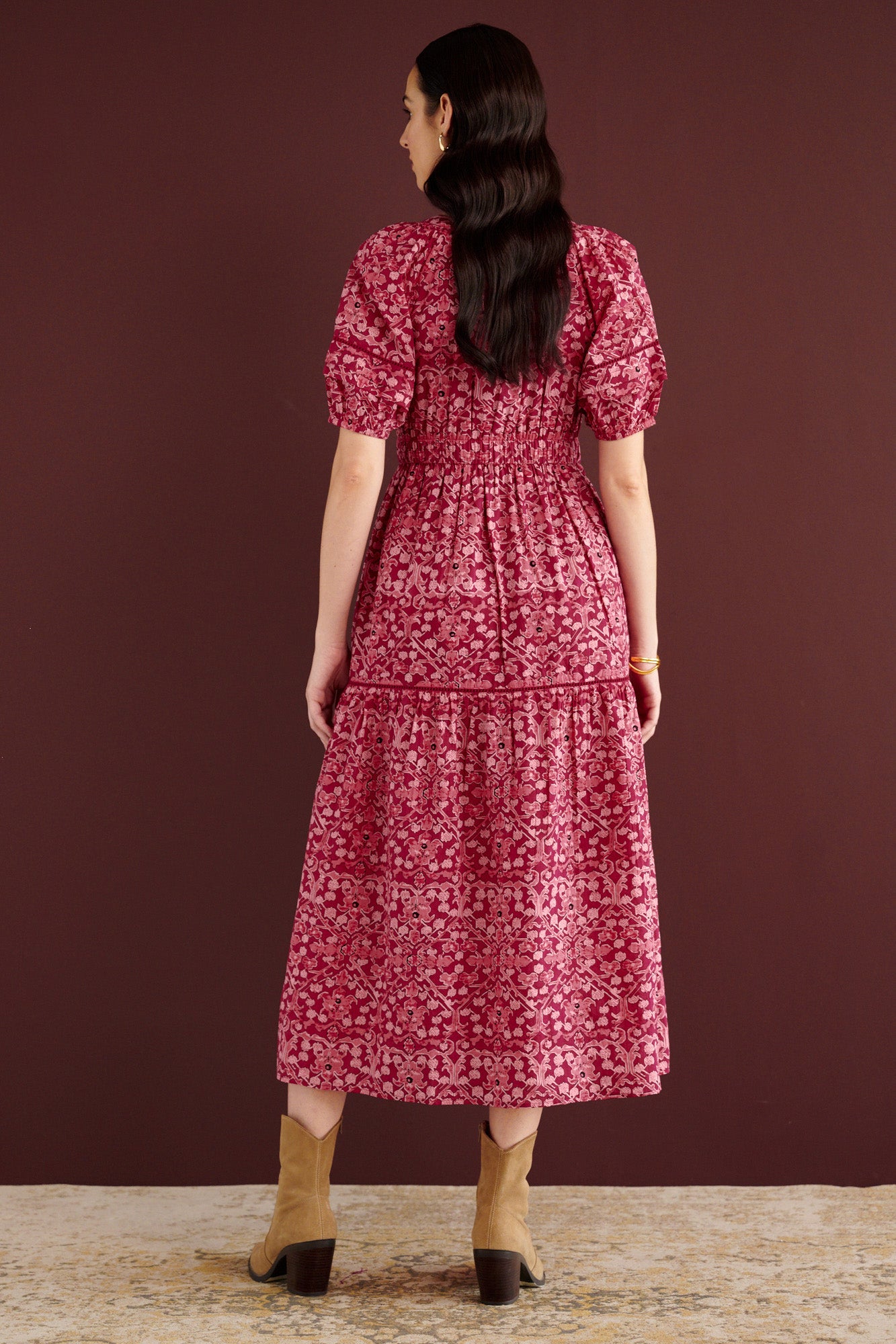 Back view of woman standing. She is wearing the Selma full-length V-neck dress in Ottoman print, with tie-neck, elastic waist, lace insets at skirt and sleeves, smooth cotton cambric, side-seam pockets, and fully lined construction.