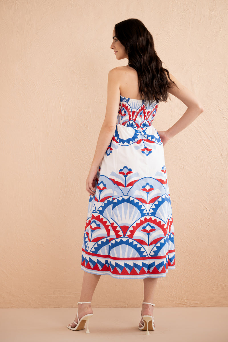 Back view of woman wearing strapless Simona dress in red, white, and blue Paros Tile print, featuring boned bodice, full gathered skirt, side pockets, and back zipper.