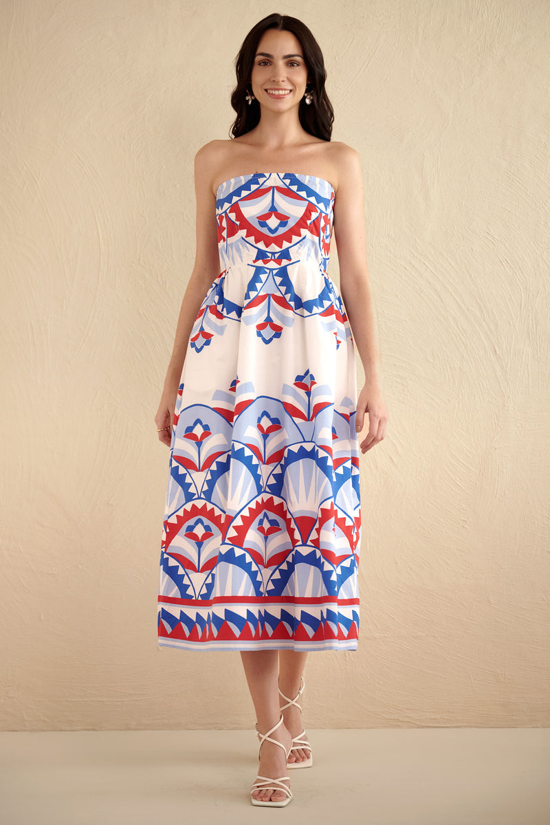 Front view of woman wearing strapless Simona dress in red, white, and blue Paros Tile print, featuring boned bodice, full gathered skirt, side pockets, and back zipper.