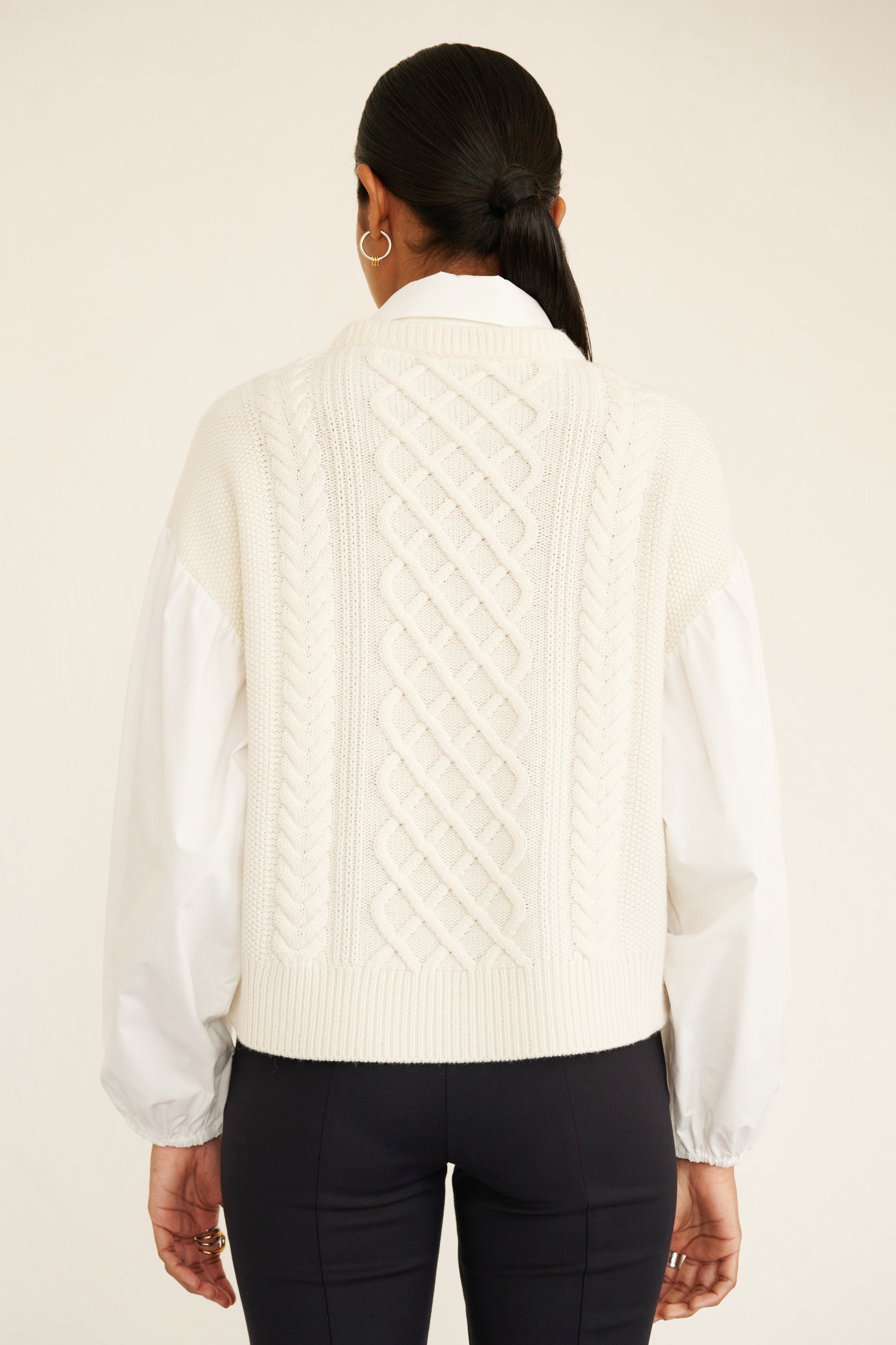 Back view of woman wearing a cable knit sweater with poplin shirt collar and sleeves, featuring elastic cuffs for shape and a layered look.