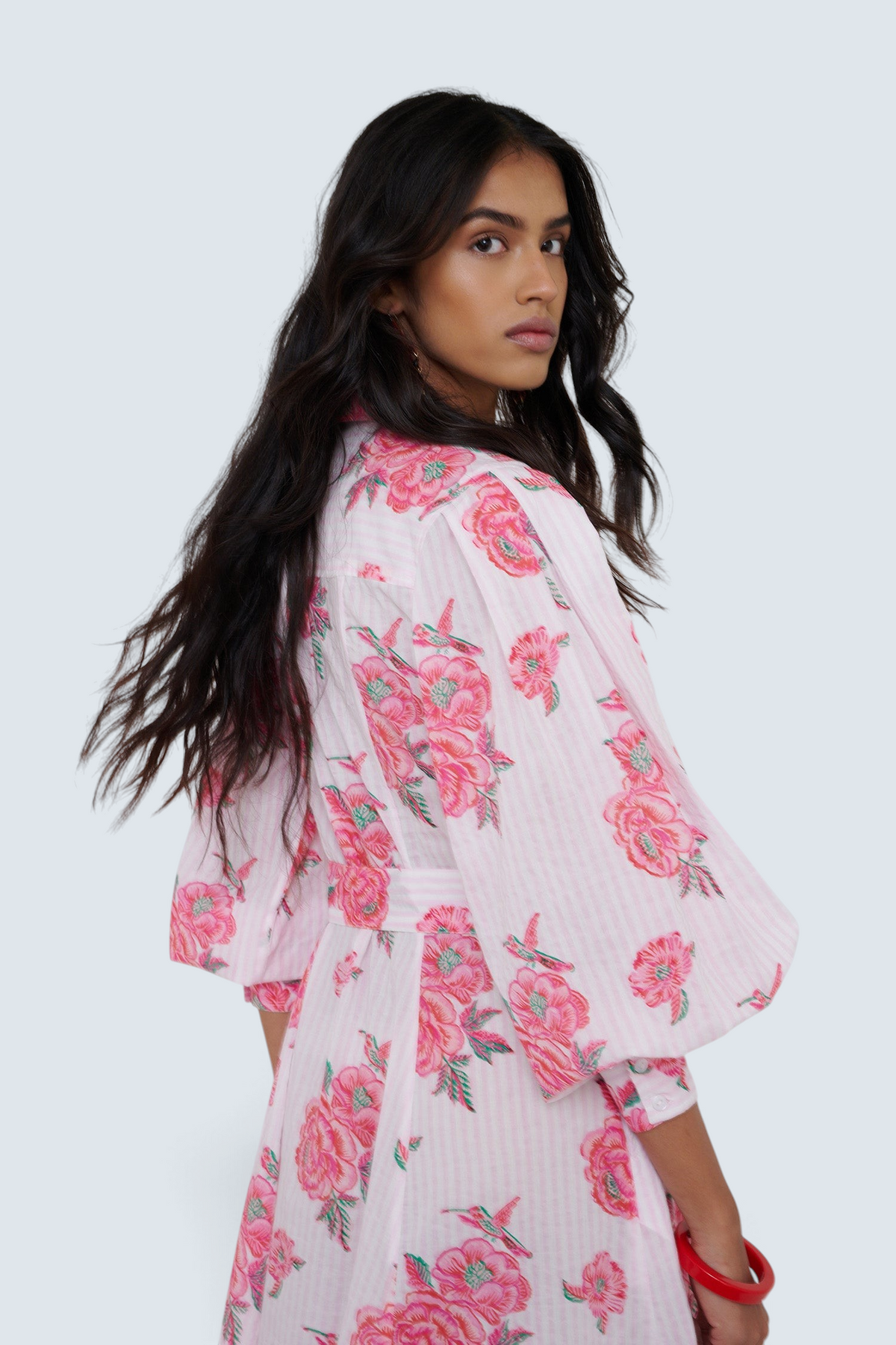 Woman wearing a white kimono-style garment with pink floral patterns on a plain background