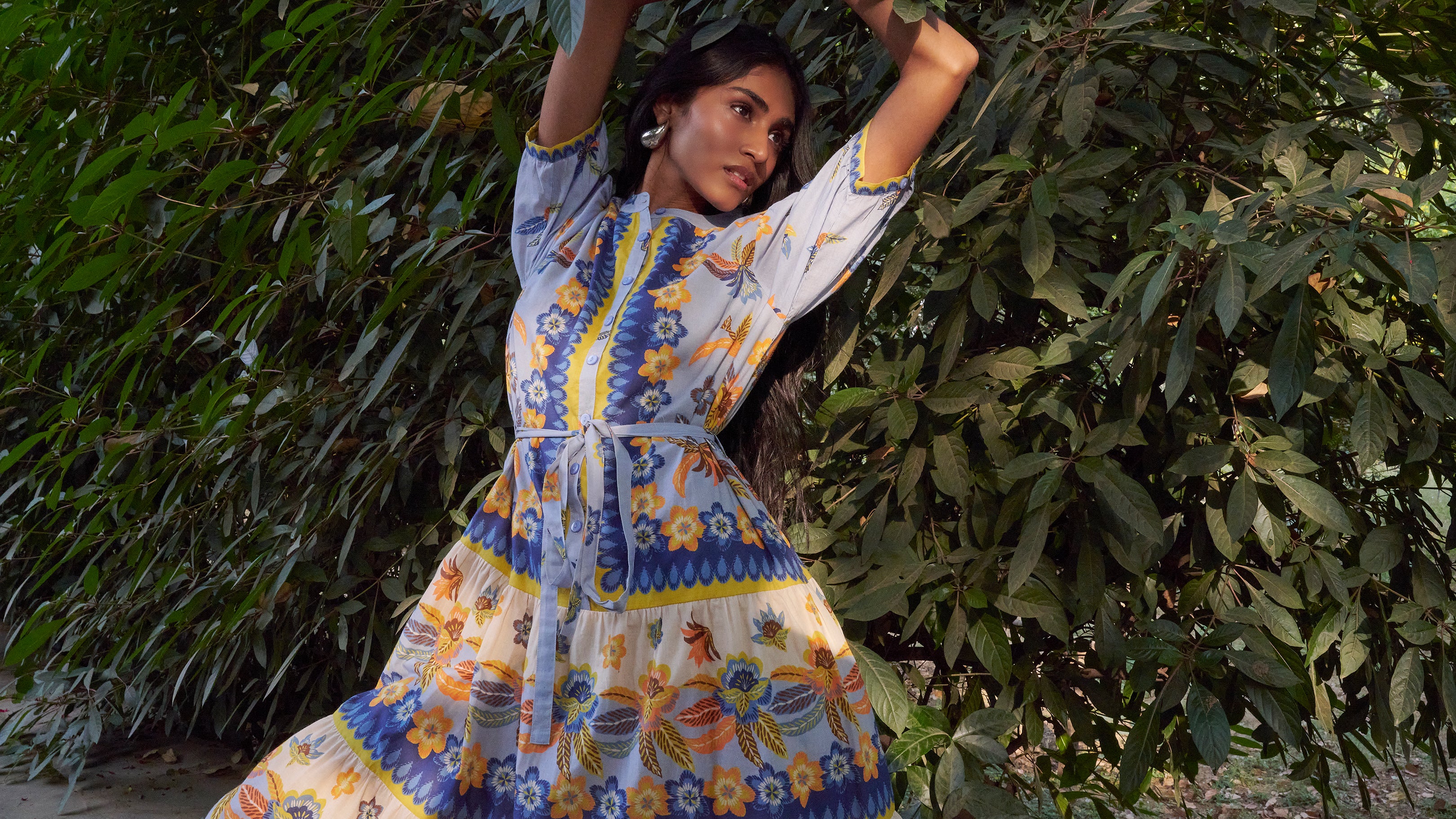 Close of model posing in front of green tree wearing Saylor Dress in Electra Floral Amberglow print.