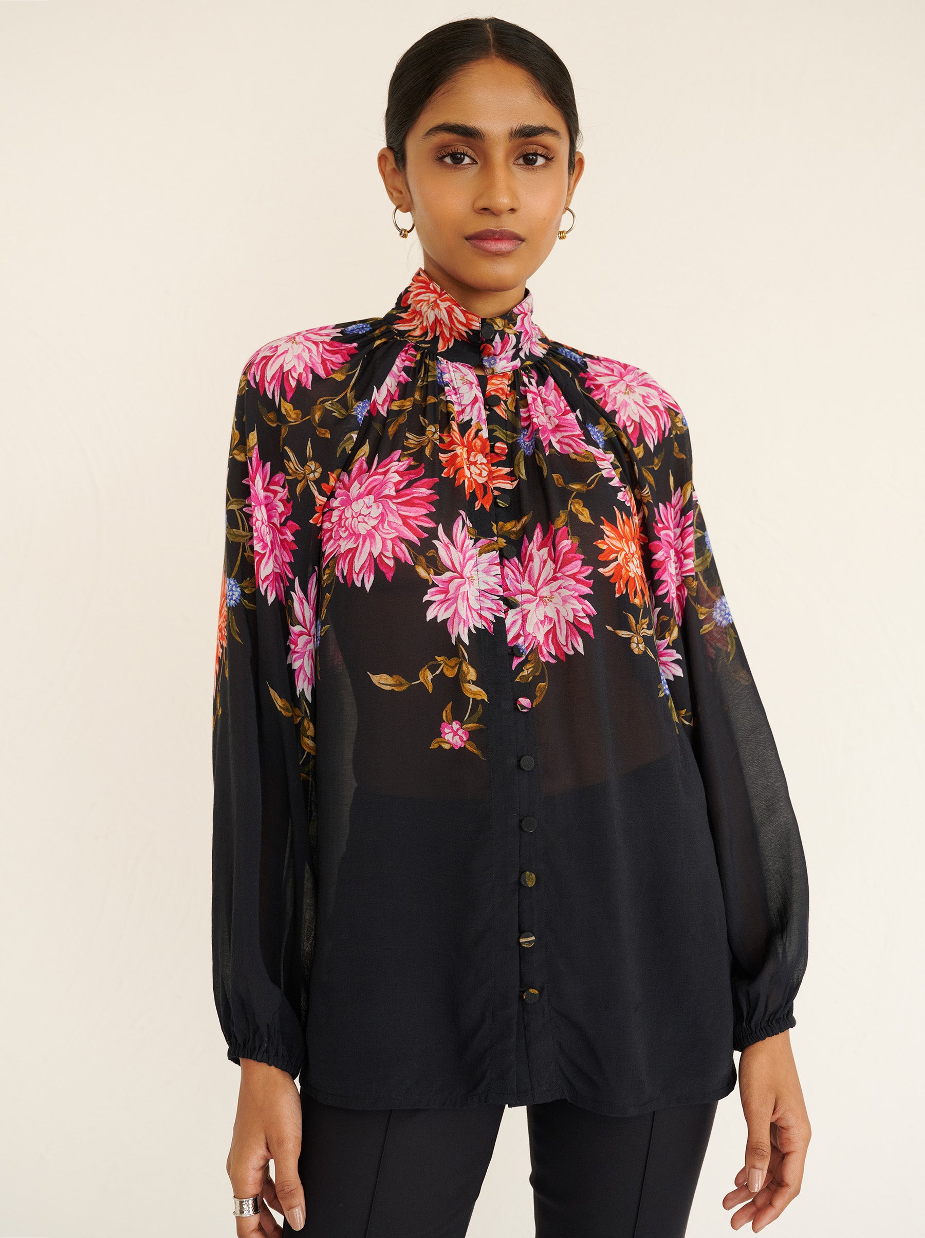 Front view close up of a model standing. She is wearing the Tara shirt in lightweight viscose voile with the Dahlia floral print. It is featuring a Victorian-style stand collar and fabric-covered buttons down the front.