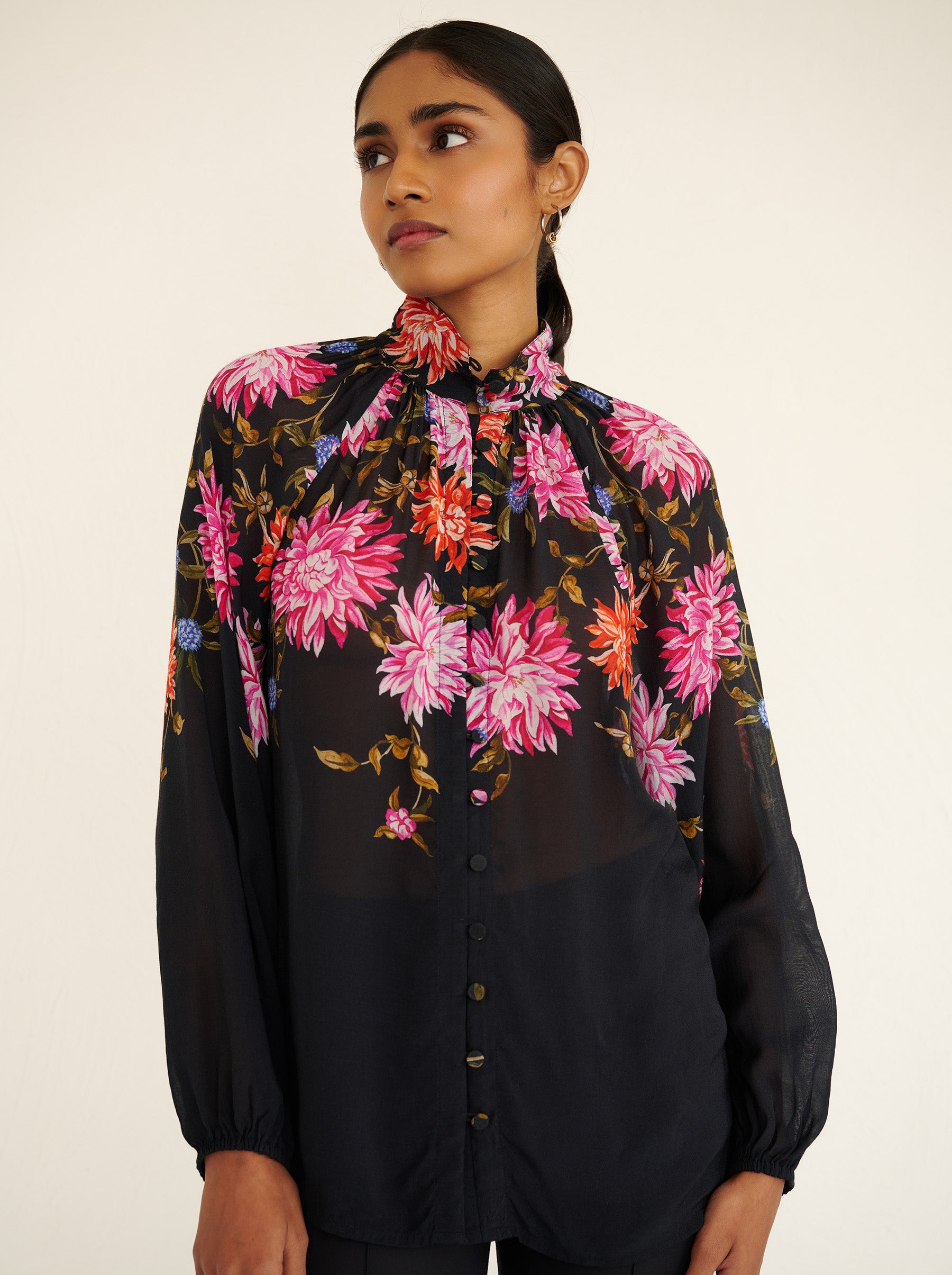 Front view close up of a model standing. She is wearing the Tara shirt in lightweight viscose voile with the Dahlia floral print. It is featuring a Victorian-style stand collar and fabric-covered buttons down the front.
