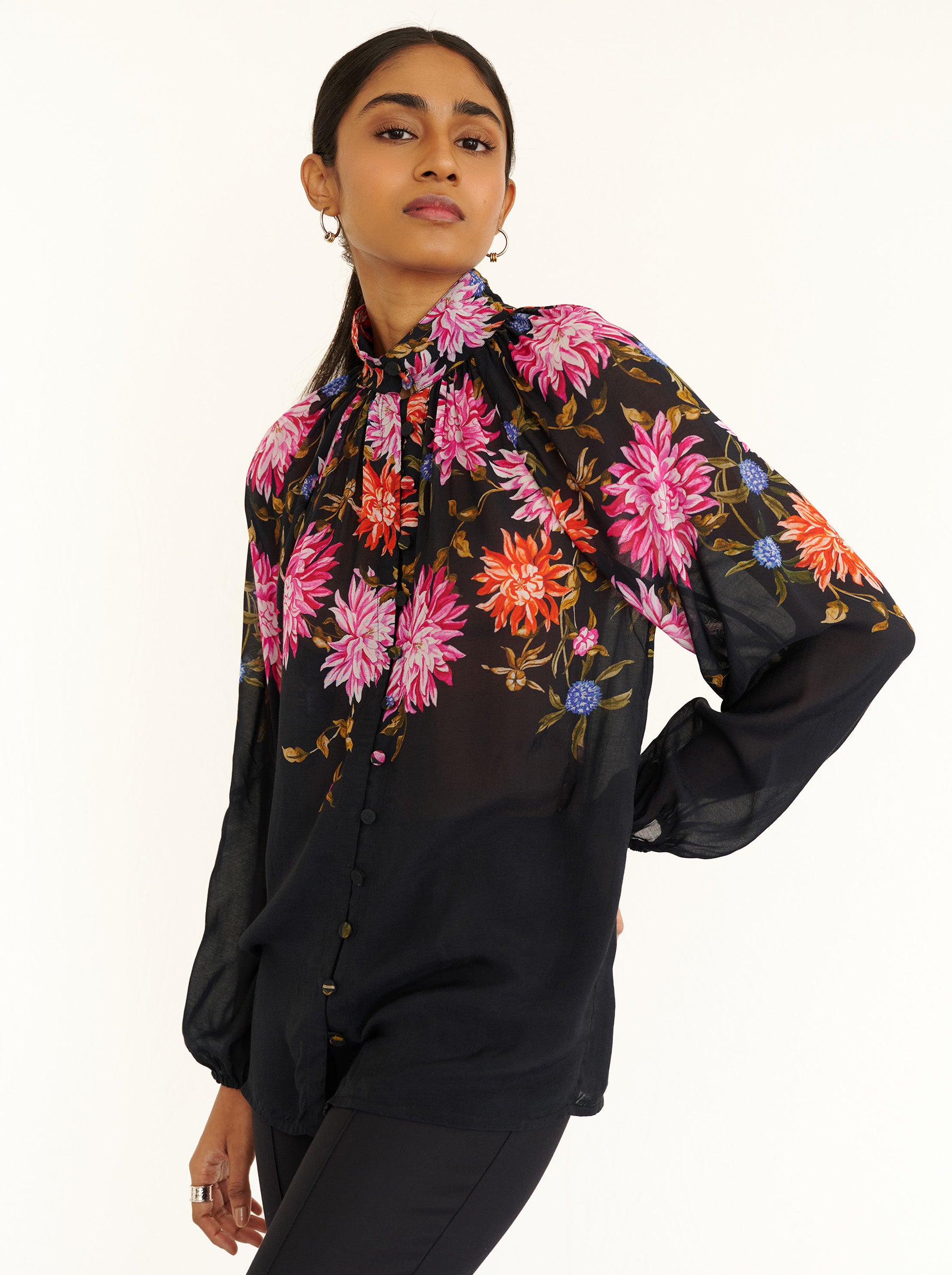 Front side view close up of a model standing. She is wearing the Tara shirt in lightweight viscose voile with the Dahlia floral print. It is featuring a Victorian-style stand collar and fabric-covered buttons down the front.
