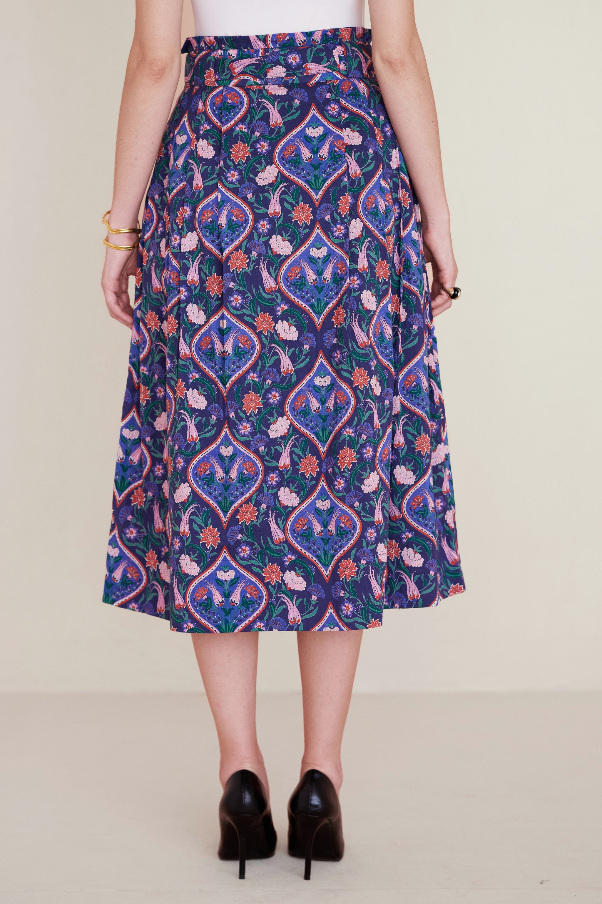 Back view of woman wearing Tobias Skirt in Persian Tile print, Lapis color. Its a midi skirt with a paperbag waist, fabric belt, and pockets, featuring a floral tile print inspired by decorative arts.