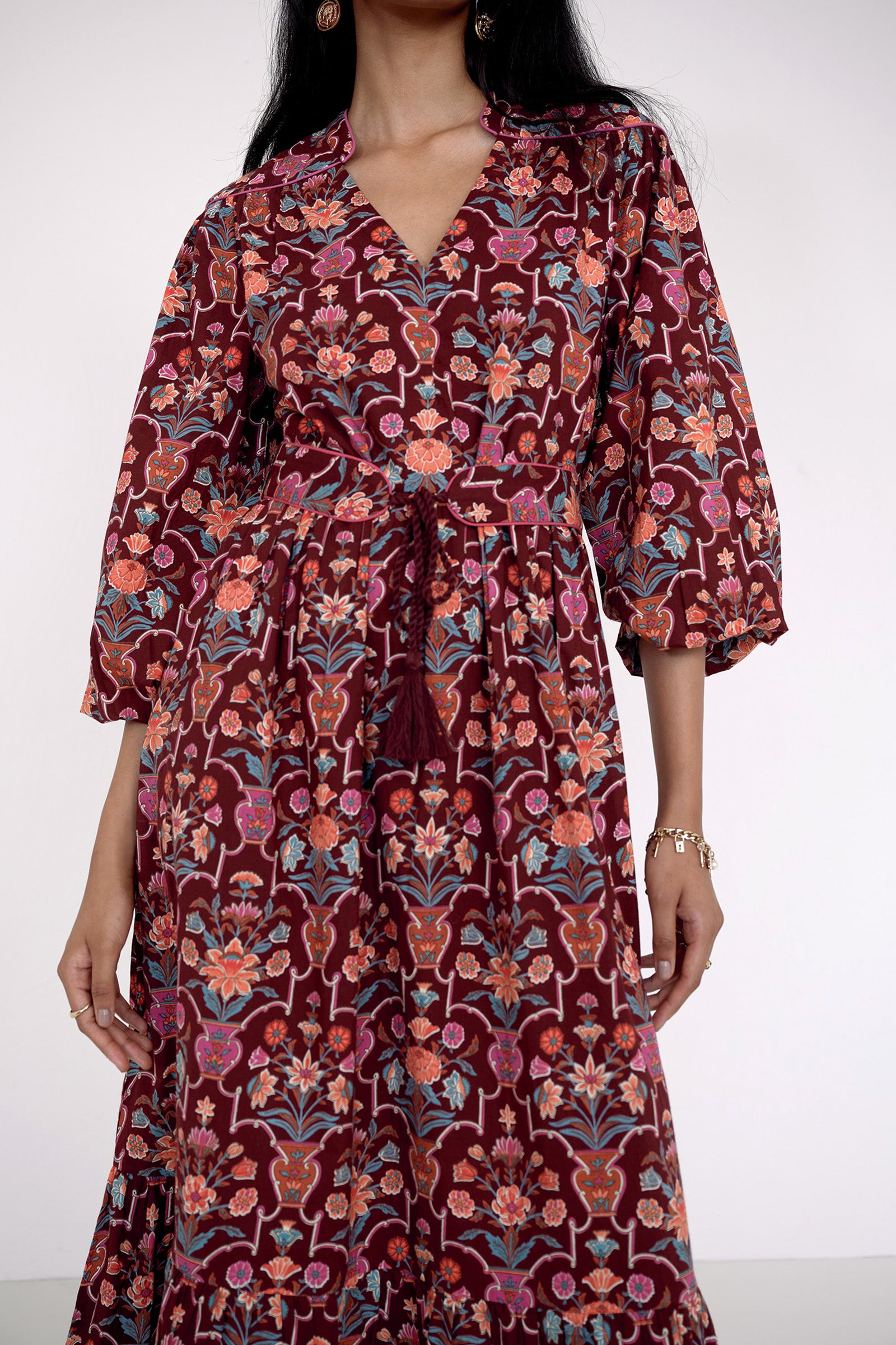Front view close up of model standing wearing the Victoria dress in Floral Vase print. It features quilted shoulder details, piping, a tassel waist tie, and an easy silhouette.