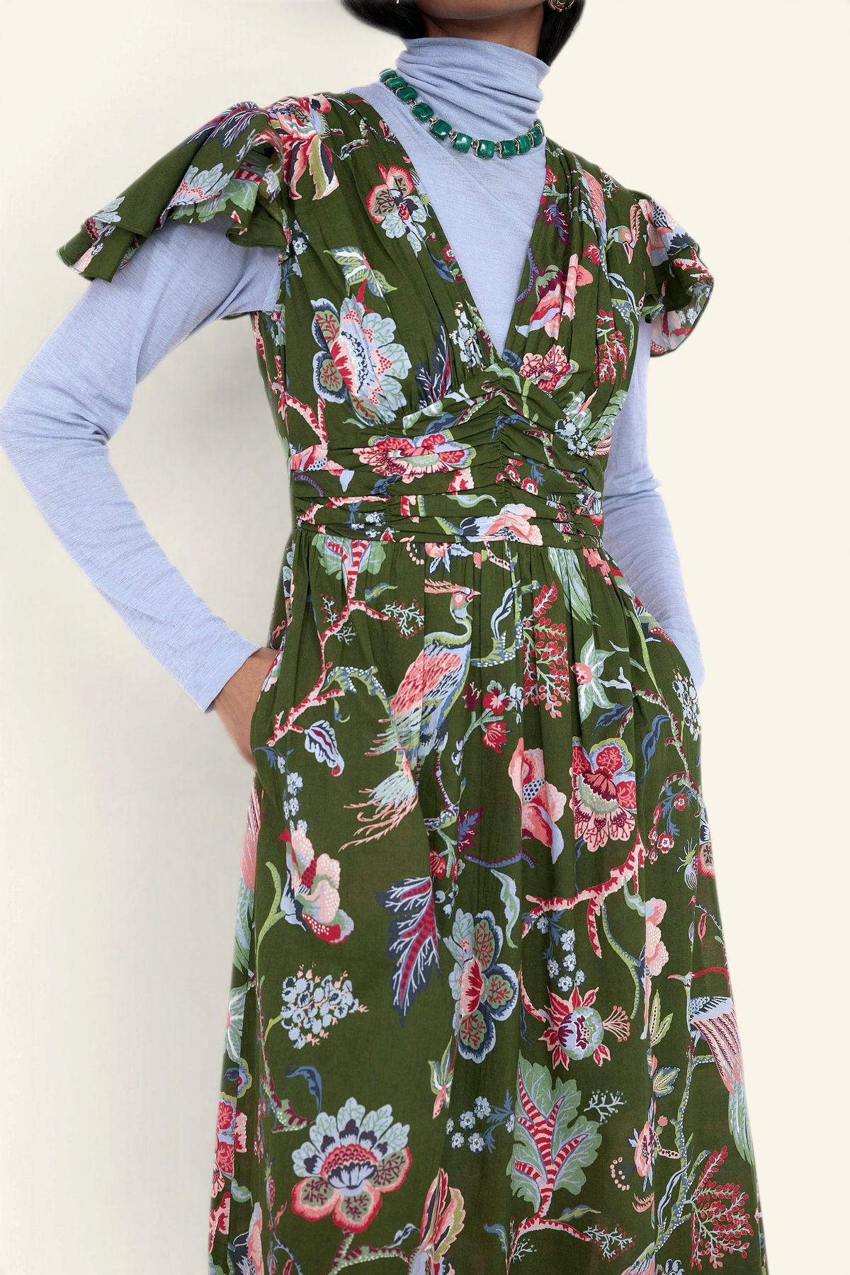 Banjanan Adele dress in moss green chintz floral print with v-neck, flutter sleeves, and pockets, worn over a turtleneck