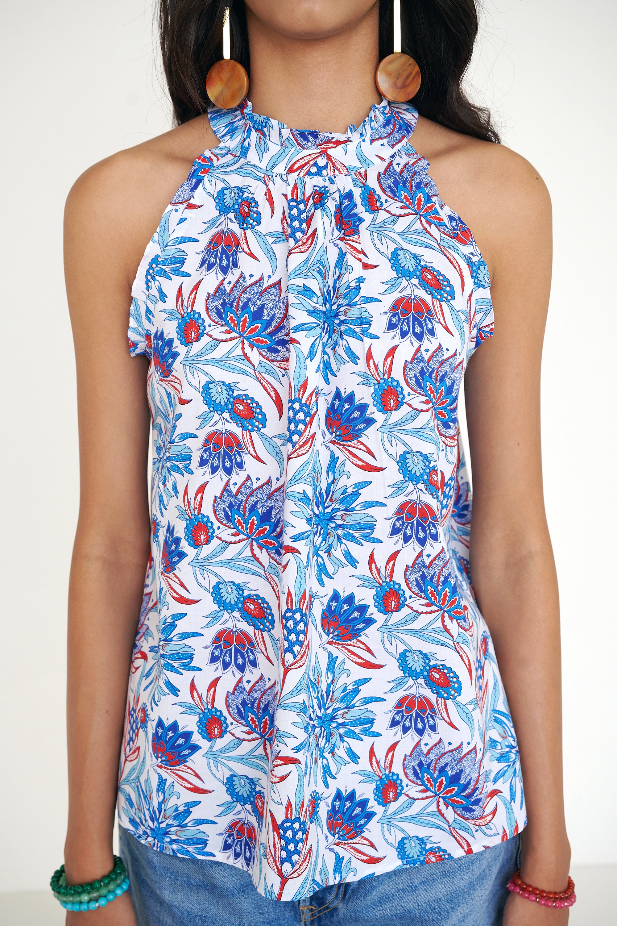 Front view close up of woman standing wearing the Amy top in the Philippa print, featuring a sleeveless silhouette, subtle ruffle neckline, and a red, white, and blue wildflower pattern. Paired with denim shorts.