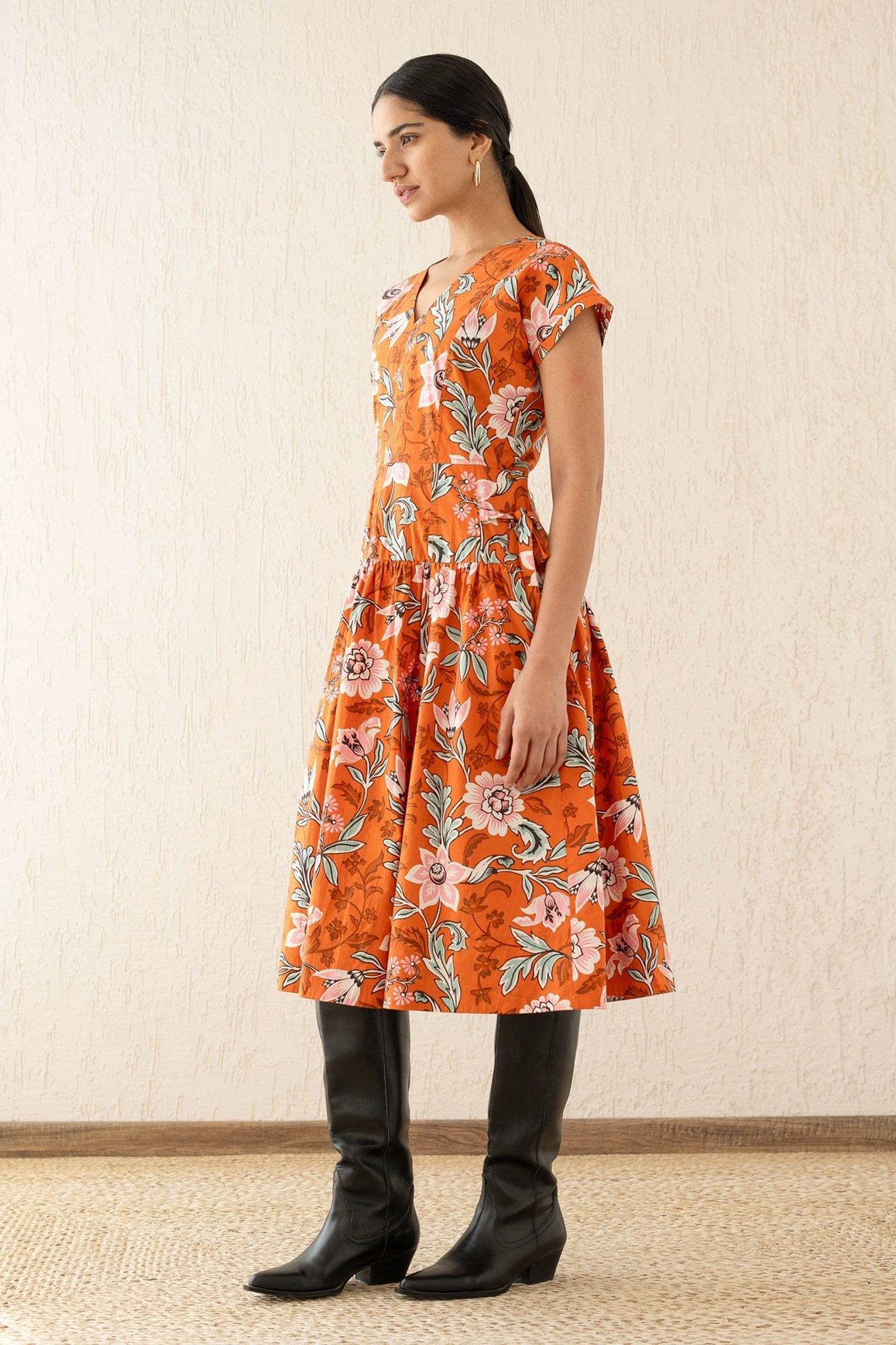 Side view of model wearing the Angela dress with a V-neck, drop waist, side ties, and bold floral print, made from cotton poplin. Perfect for layering in autumn.