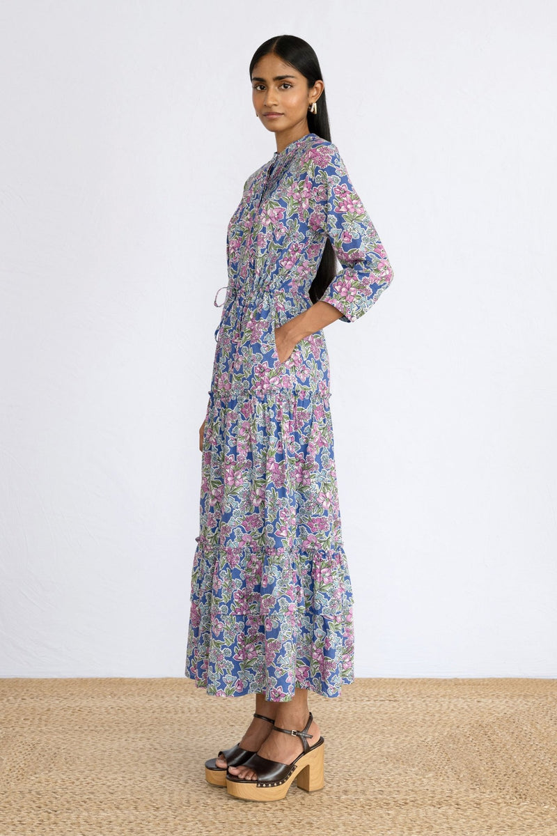 Side view of model wearing a full length Bazaar Dress Arcadia Dazzling Blue with a hand in pocket.