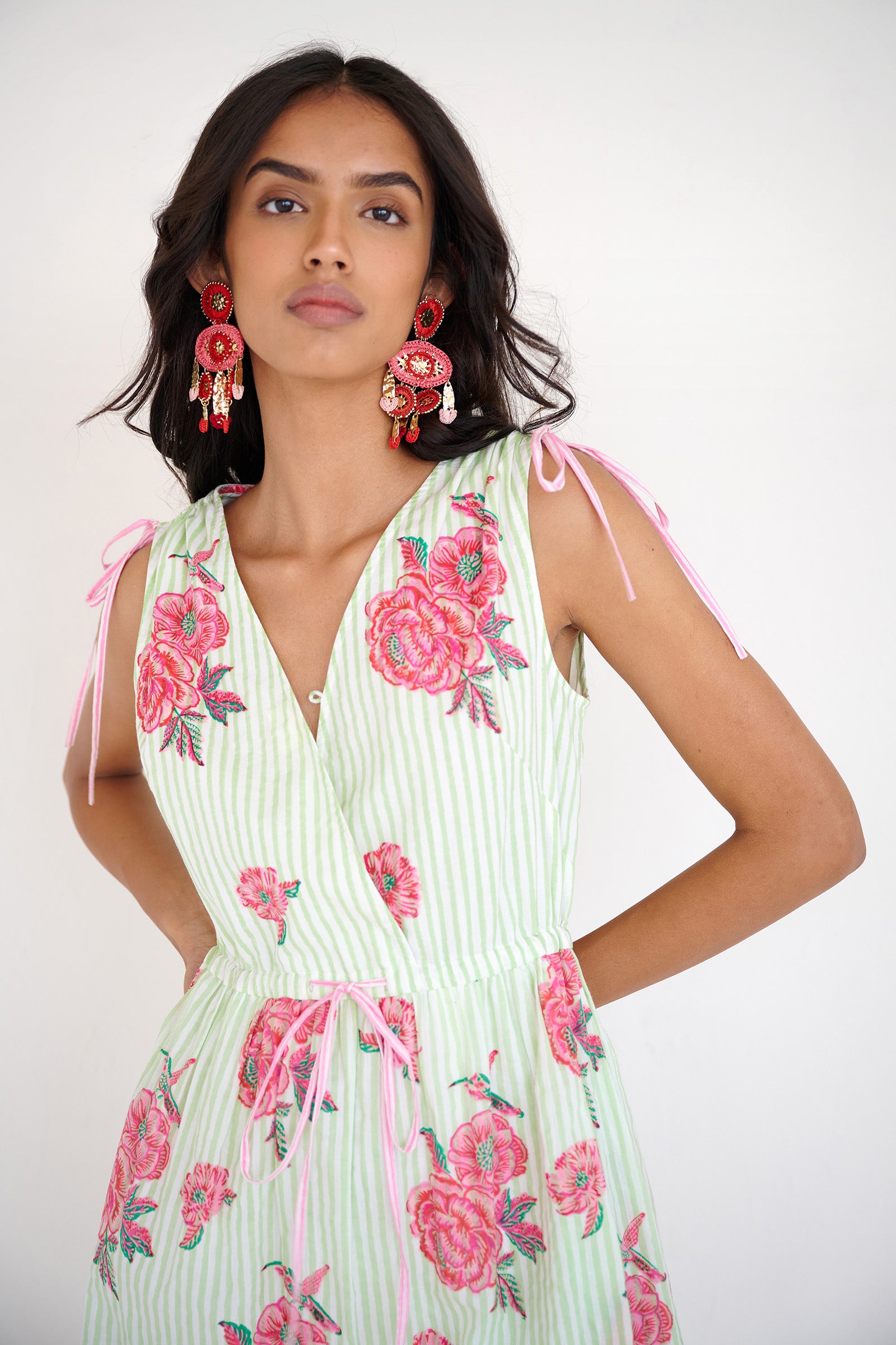 Front view close up of woman standing. She is wearing the Becca dress in the Eliza Rose print, featuring an adjustable waist, shoulder ties, a deep V-neckline, and hand block-printed floral motifs with hummingbird details.