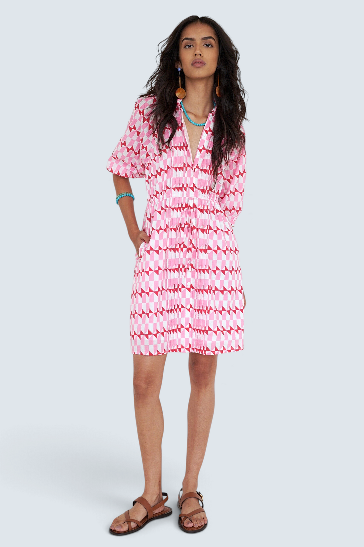 Front view of woman standing. She is  wearing the Benita dress in the Stevie print, featuring a shirtdress silhouette, button-front placket, drawstring waist, and geometric motifs inspired by the French Riviera.