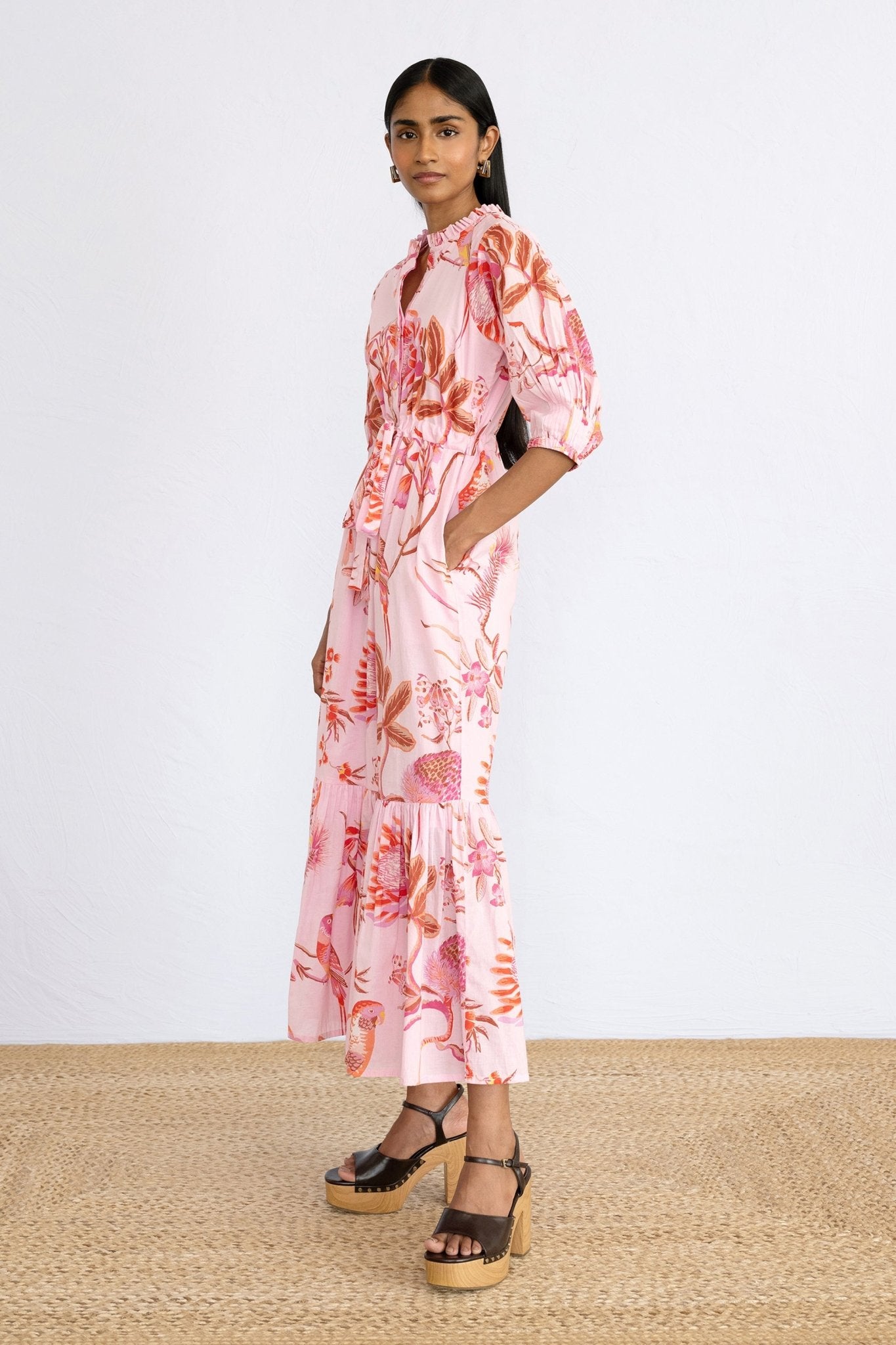 Side view of model standing wearing Betty Dress in Botany Bay Pink Mist print with a hand in pocket.