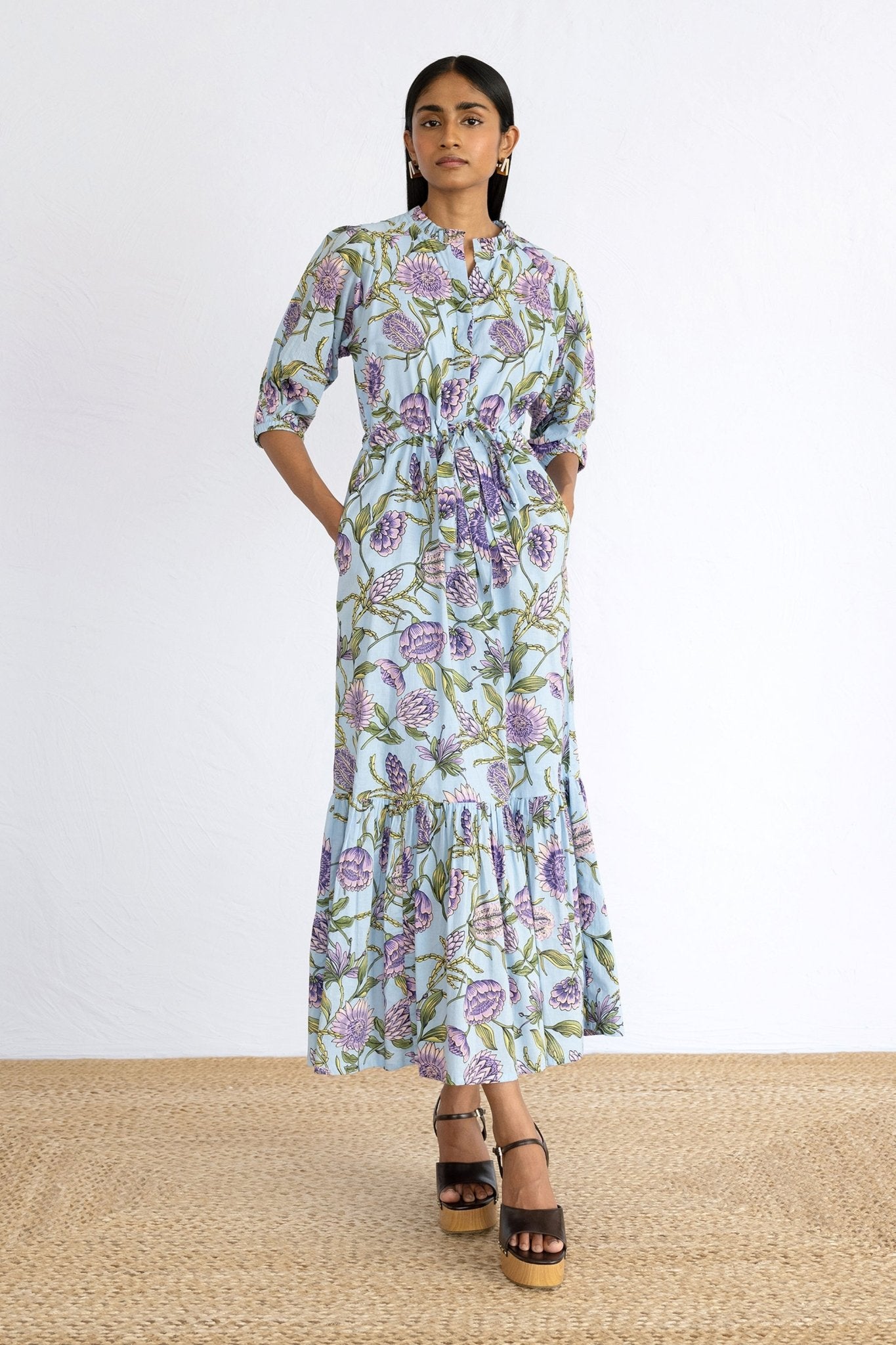 Front view of model wearing Betty Dress in Protea Orchid print with hands in pocket. 