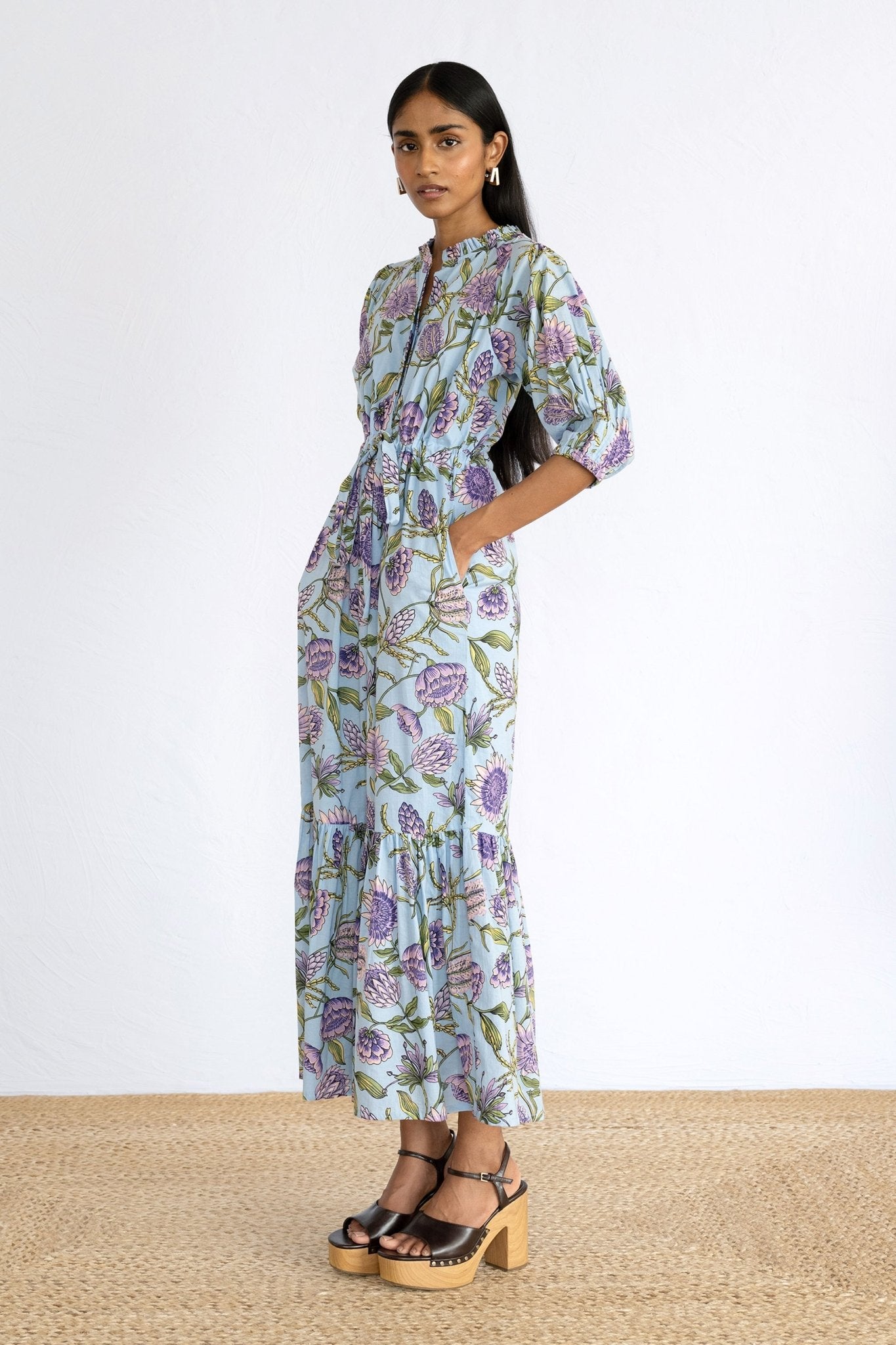 Side view of model wearing Betty Dress in Protea Orchid print with hands in pocket. 