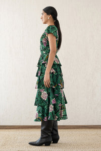 Side view of a woman wearing the Brigit dress in Tartan Rose Pine print. It features a cascading skirt of tiered ruffles, pin tucks under bust and waist, a V-neck, and cap sleeves.