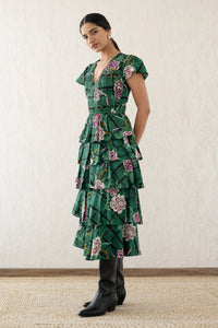 Side view of a woman wearing the Brigit dress in Tartan Rose Pine print. It features a cascading skirt of tiered ruffles, pin tucks under bust and waist, a V-neck, and cap sleeves.