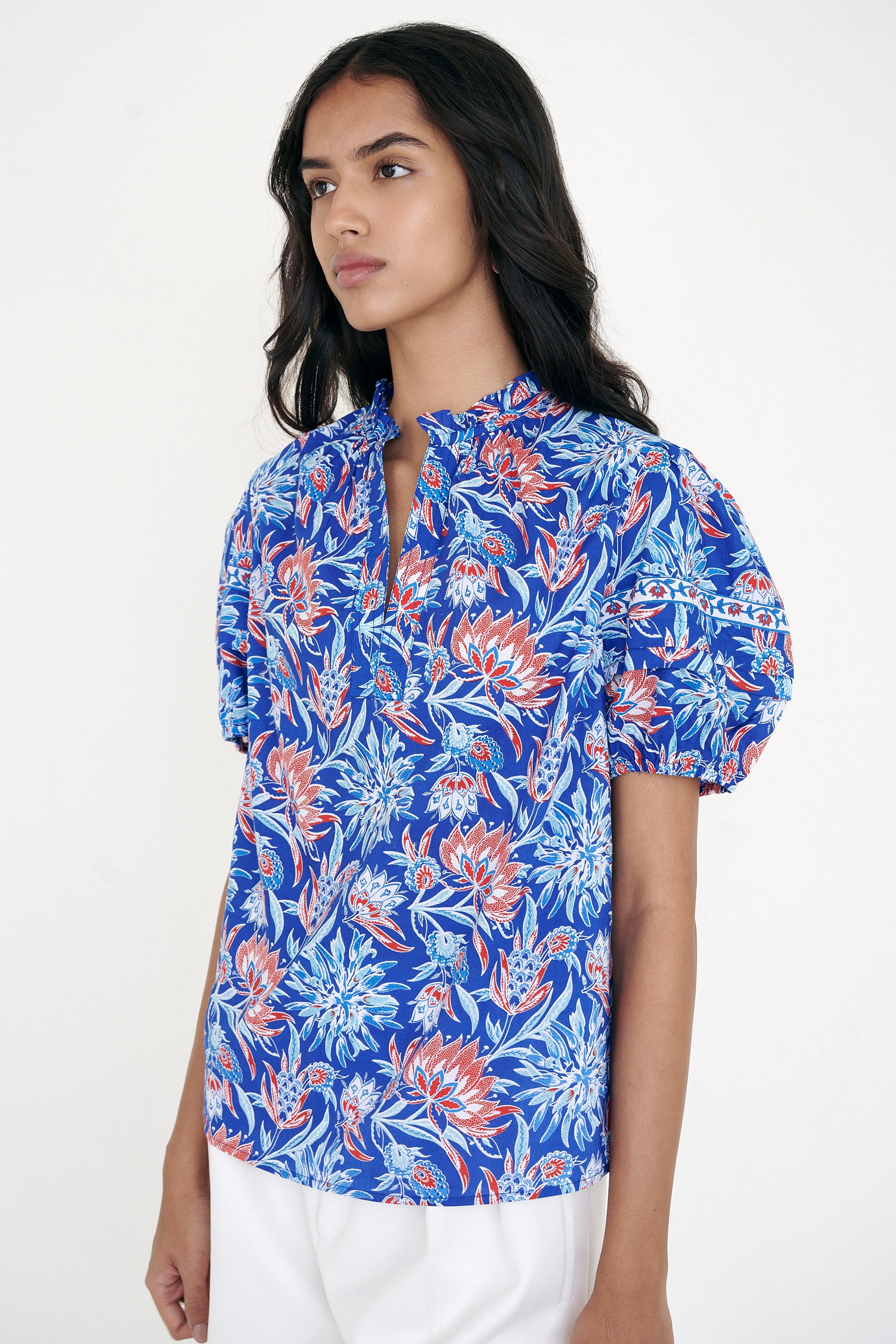 Side view of woman standing wearing the Bronte top in the Philippa print, featuring a front opening, delicate contrast trim, pleated sleeves, and a hand-screen-printed wildflower pattern.