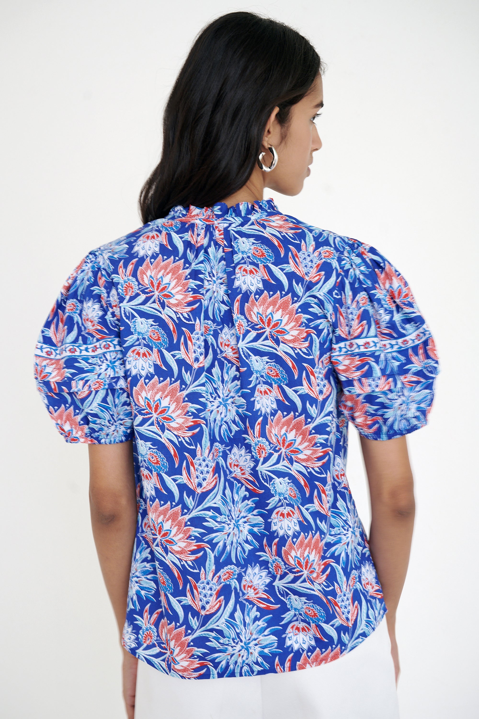 Back view of woman standing wearing the Bronte top in the Philippa print, featuring a front opening, delicate contrast trim, pleated sleeves, and a hand-screen-printed wildflower pattern.