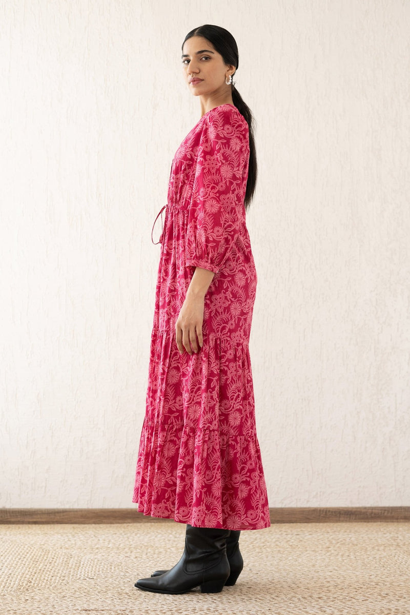 Side view of a woman wearing the Castor dress with soft puff sleeves and a gathered drawstring skirt in Tresse Winterberry print, a floral design. The dress is fully lined finished with side seam pockets.