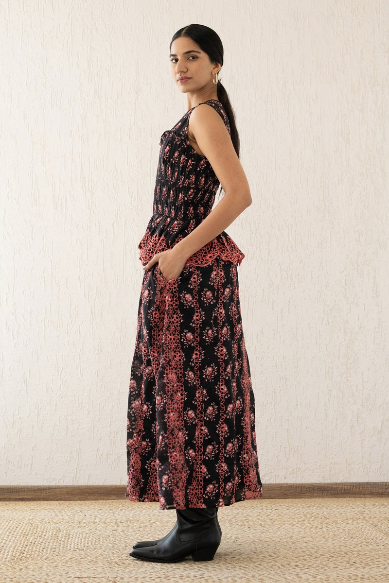 Side view of a woman wearing the Claudia midi dress sleeveless with a smocked sweetheart bodice, eyelet cutout details, and scalloped embroidery. It features the Butti Dusk print and has pockets.