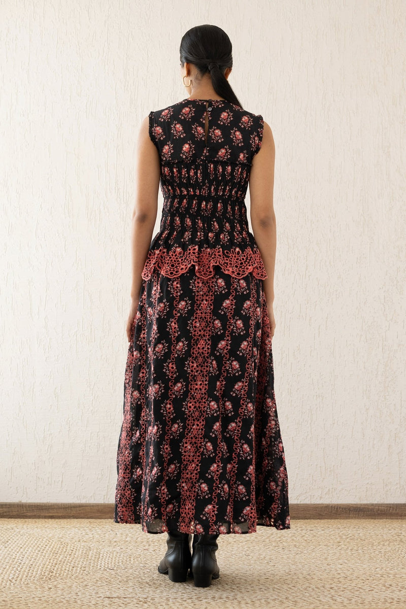 Back view of a woman wearing the Claudia midi dress sleeveless with a smocked sweetheart bodice, eyelet cutout details, and scalloped embroidery. It features the Butti Dusk print and has pockets.