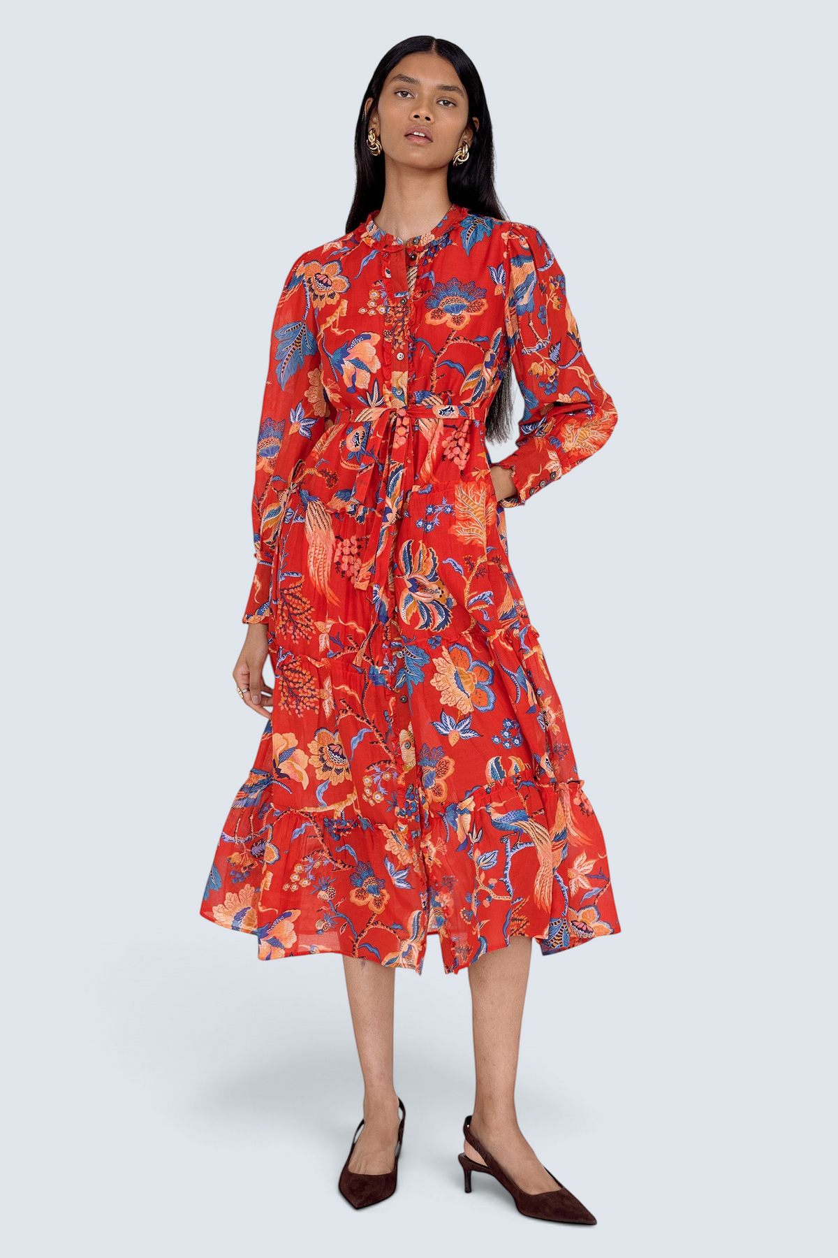 Front view of model standing. She is wearing the Emira dress in Chintz print with left hand in pocket. It features a flowing skirt, delicate ruffles, fabric-covered buttons, and a detachable belt.
